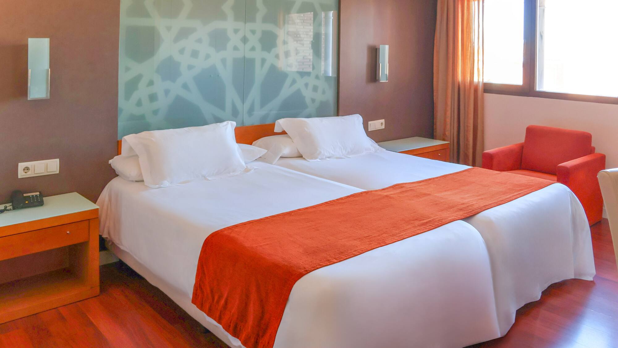 Modern hotel room with two single beds, white linen, and orange accents.