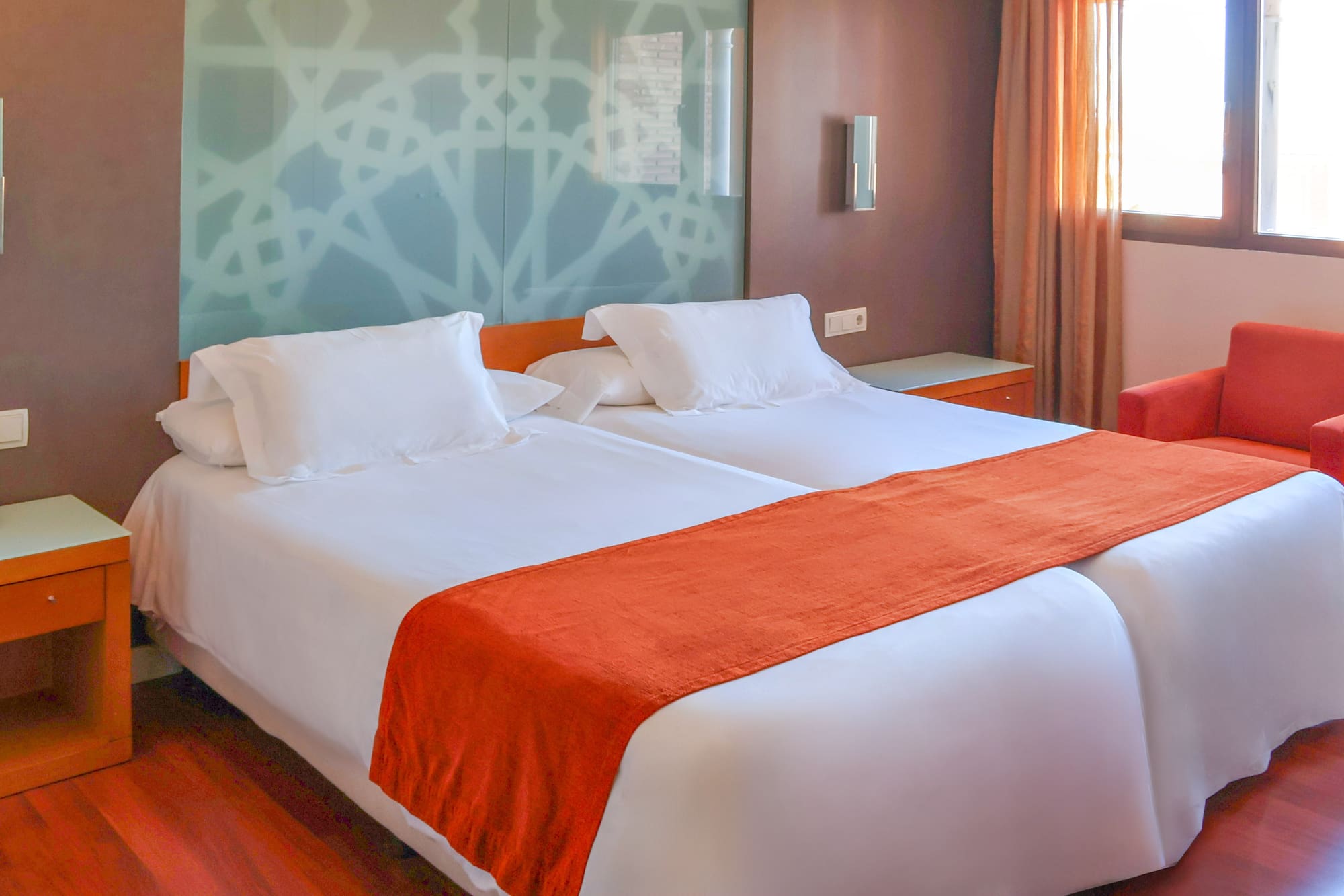 Modern hotel room with two single beds, white linen, and orange accents.