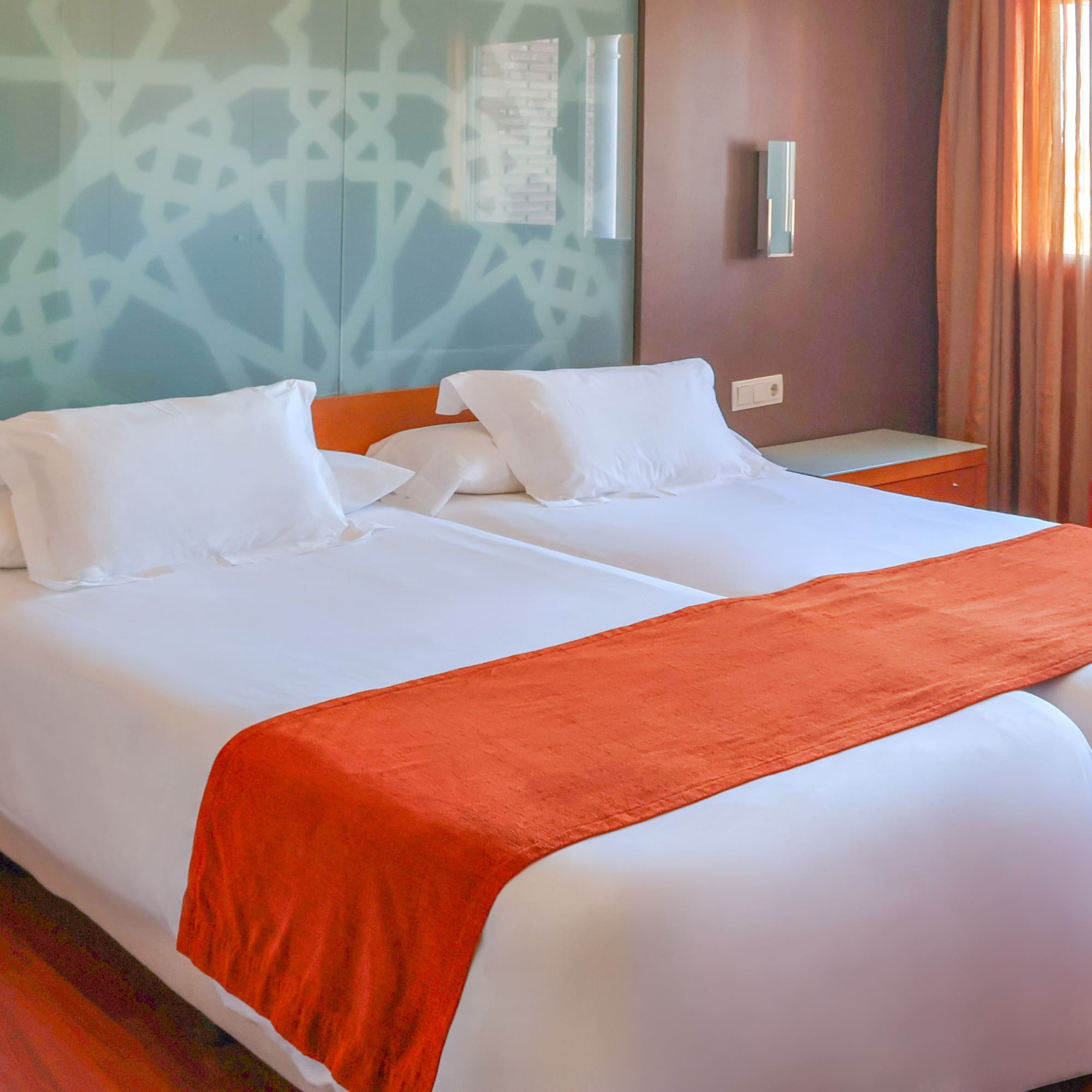 Modern hotel room with two single beds, white linen, and orange accents.