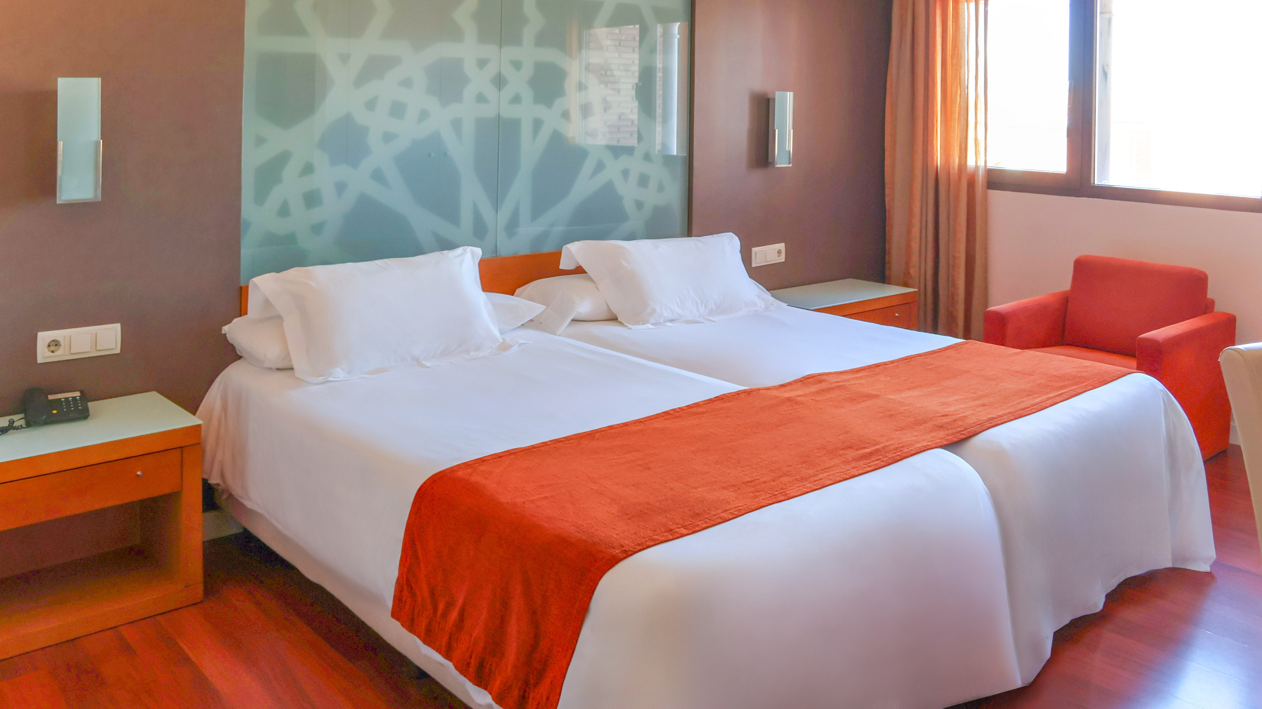 Modern hotel room with two single beds, white linen, and orange accents.