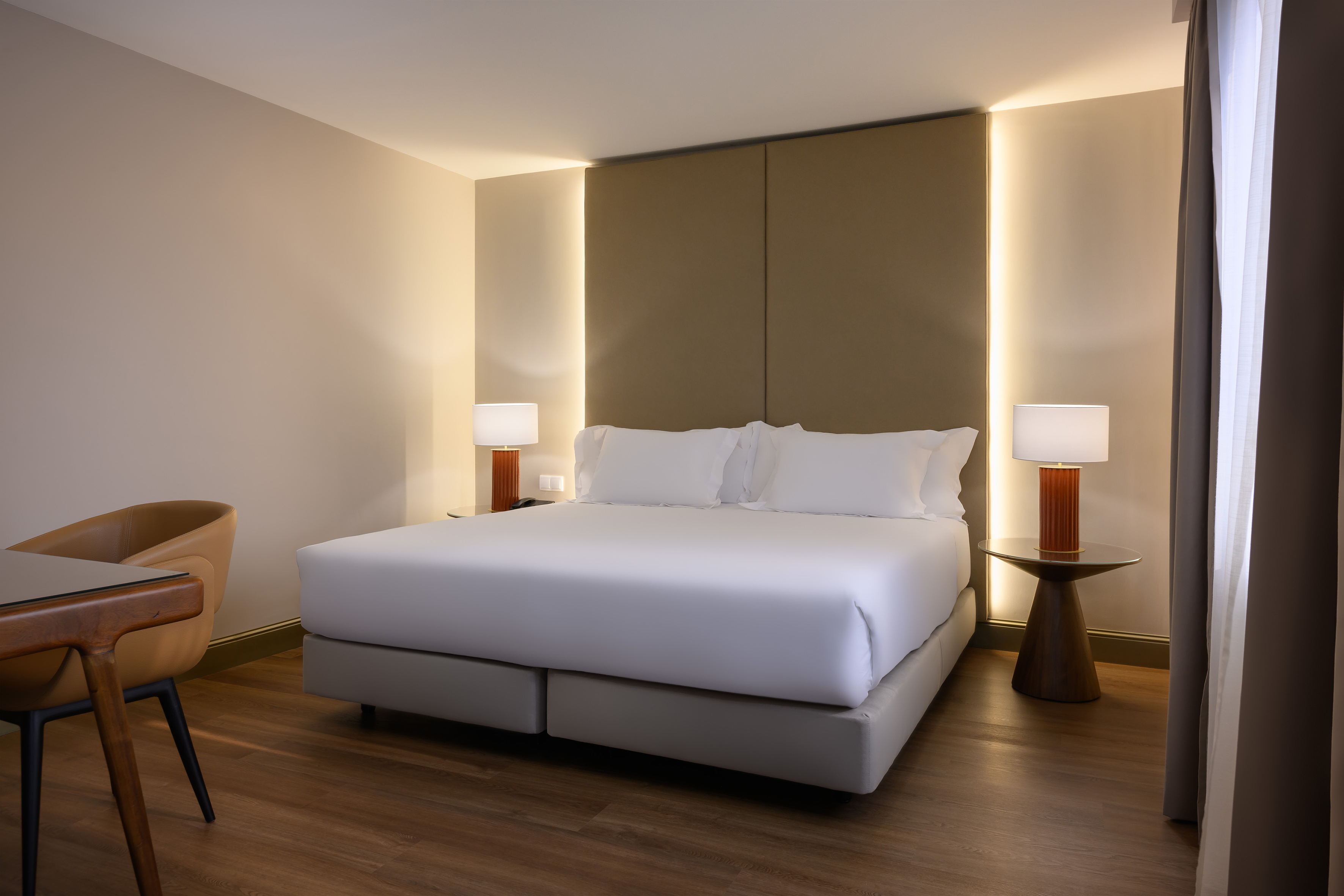 Contemporary hotel bedroom with white bed, backlit headboard, and wood flooring.