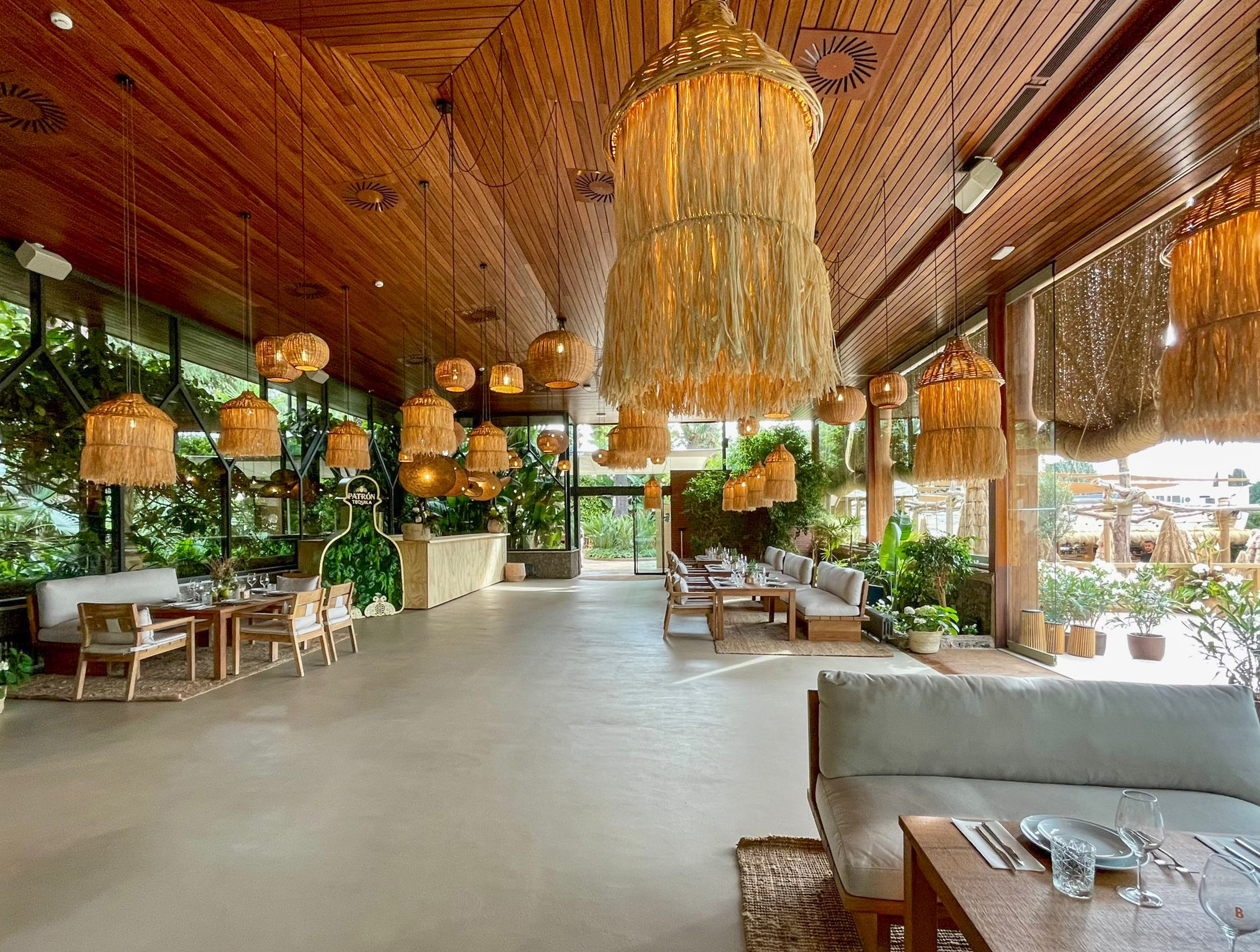 Restaurant dining room with woven lamps, wooden ceiling, and green plants.