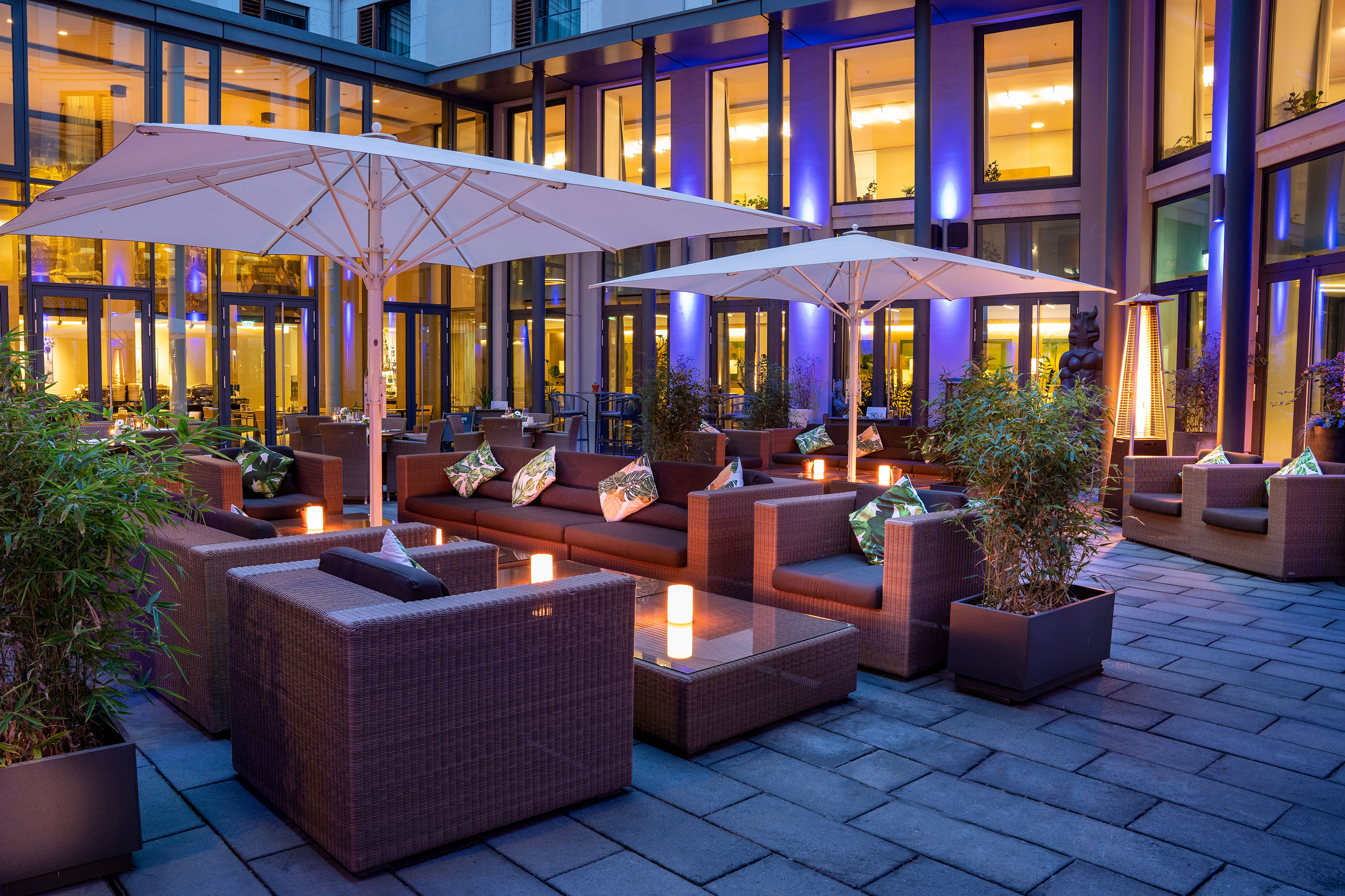 Elegant hotel patio with wicker furniture, umbrellas, and blue building lighting. - VEN Patio - Innside Dresda, Dresda