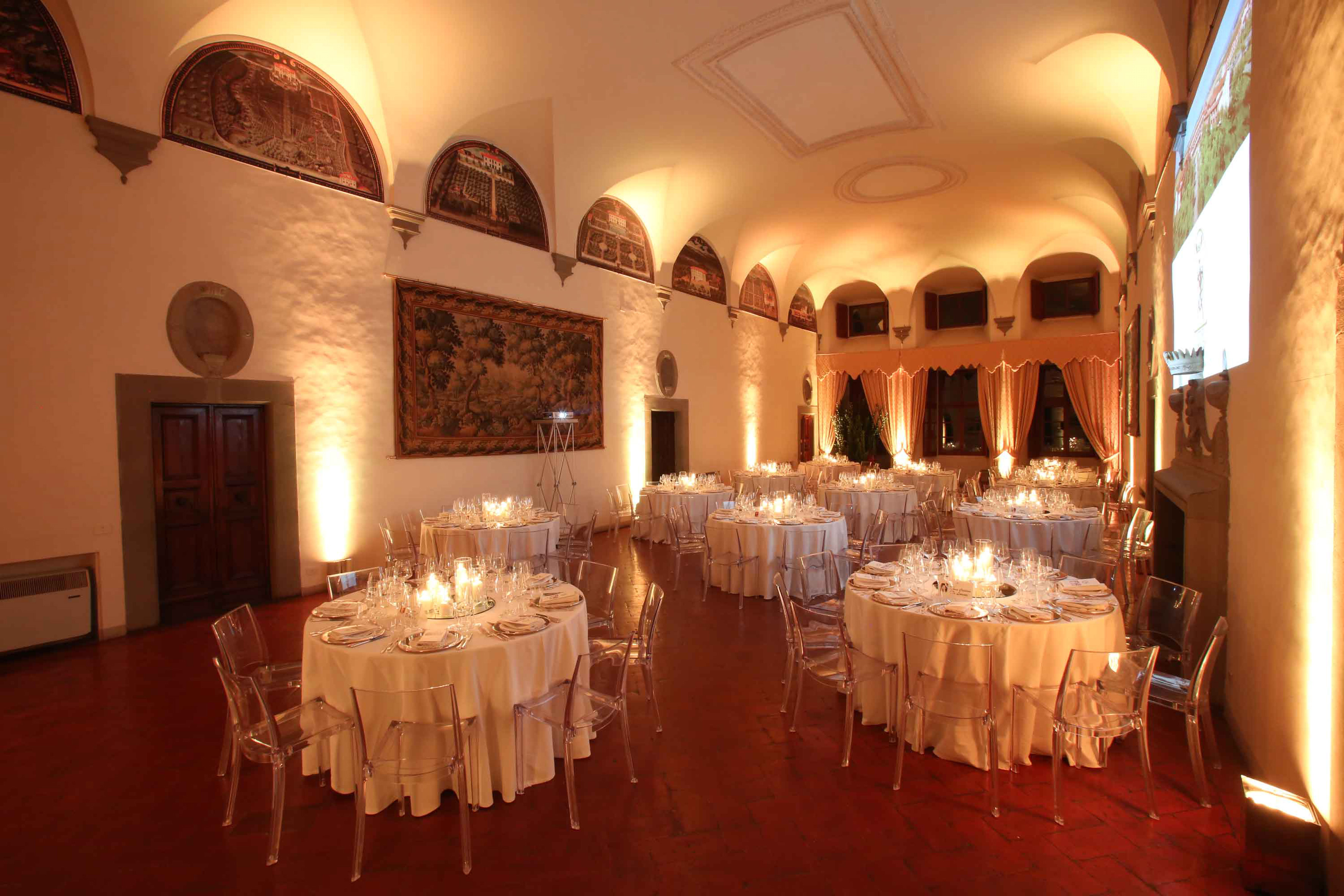 Historic banquet hall with candlelit tables, clear chairs, frescoes.