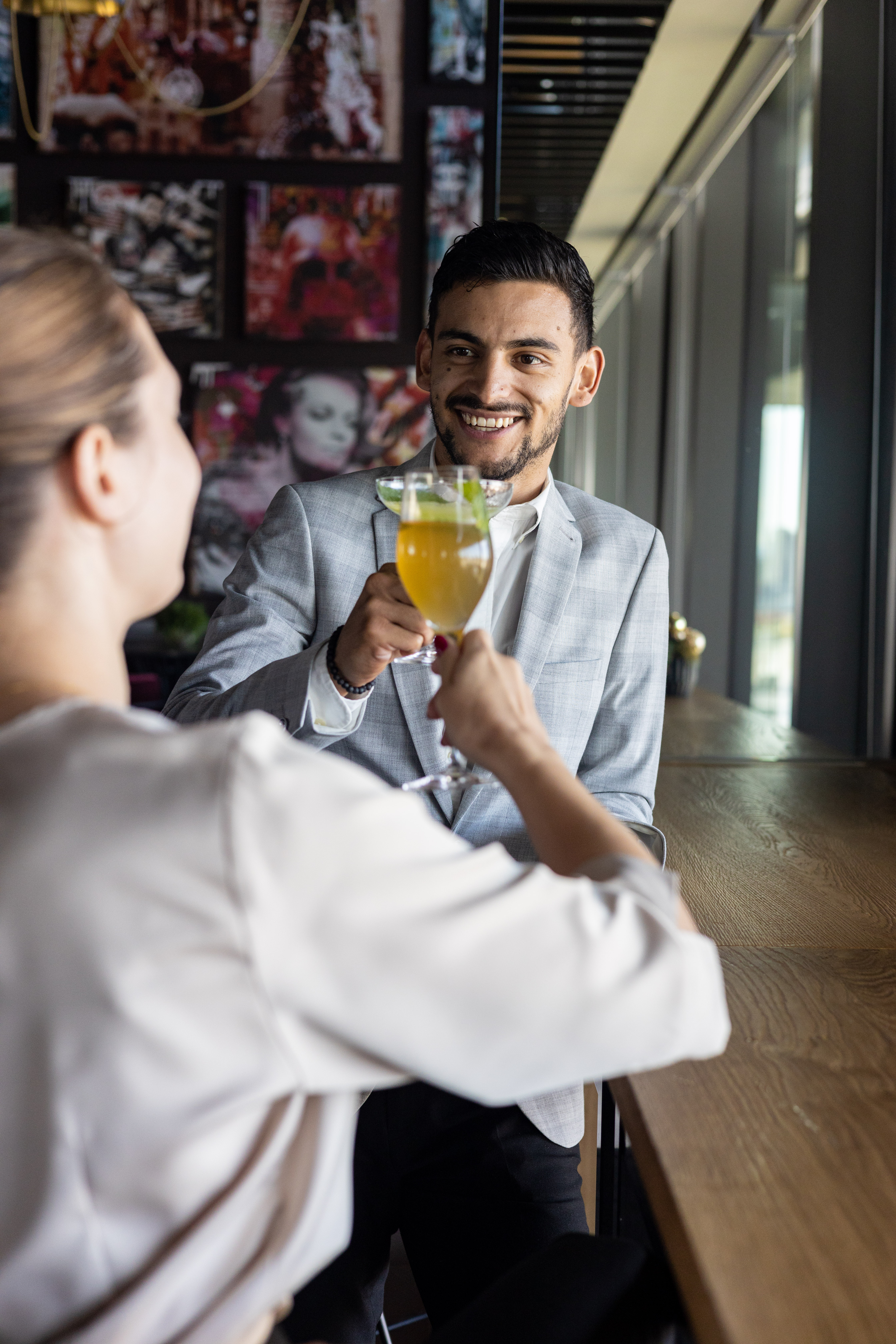 Man and woman clinking cocktail glasses, celebrating at a modern bar.