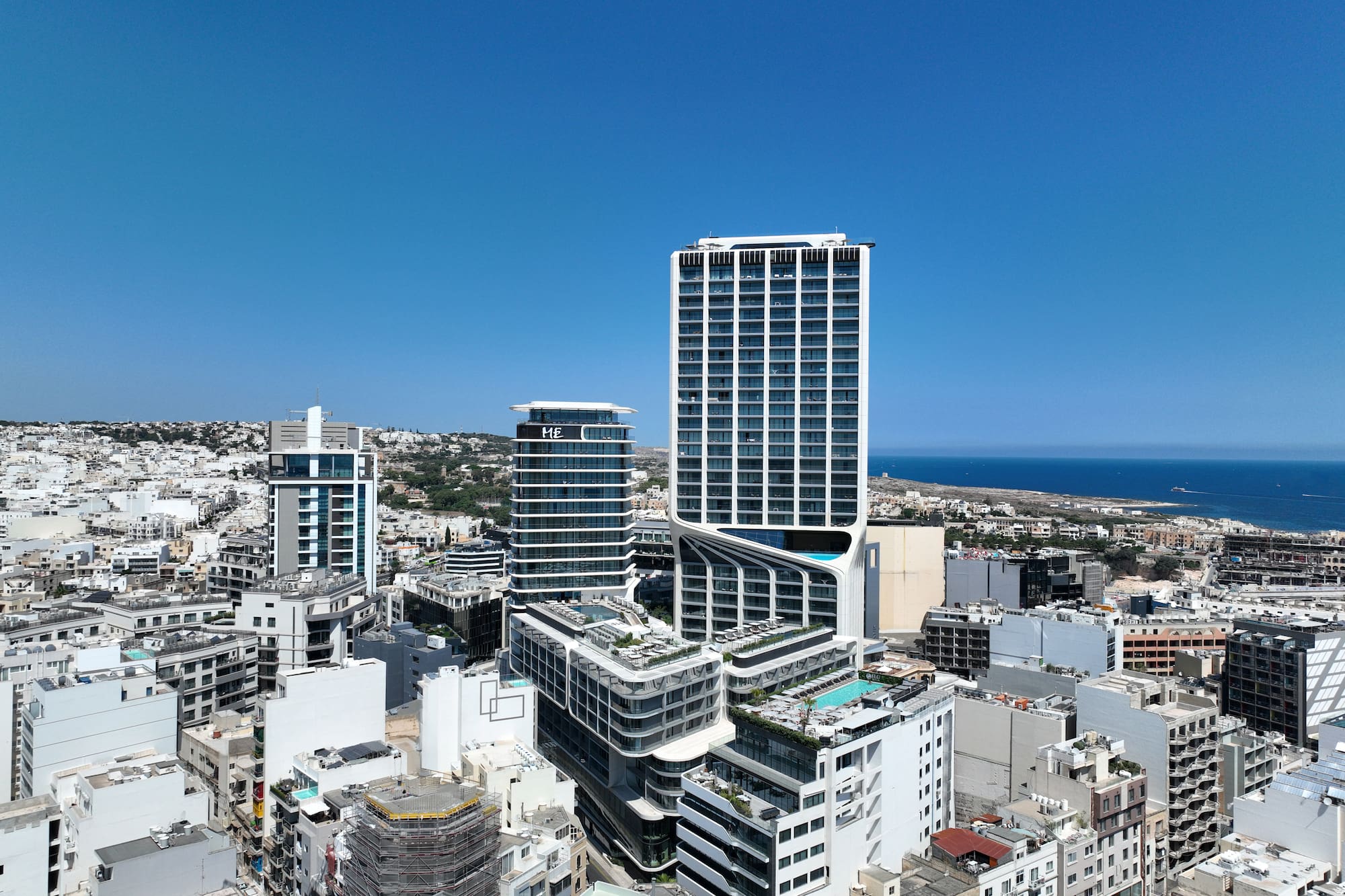 Modern high-rise hotel, rooftop pools, and city skyline with distant sea view.