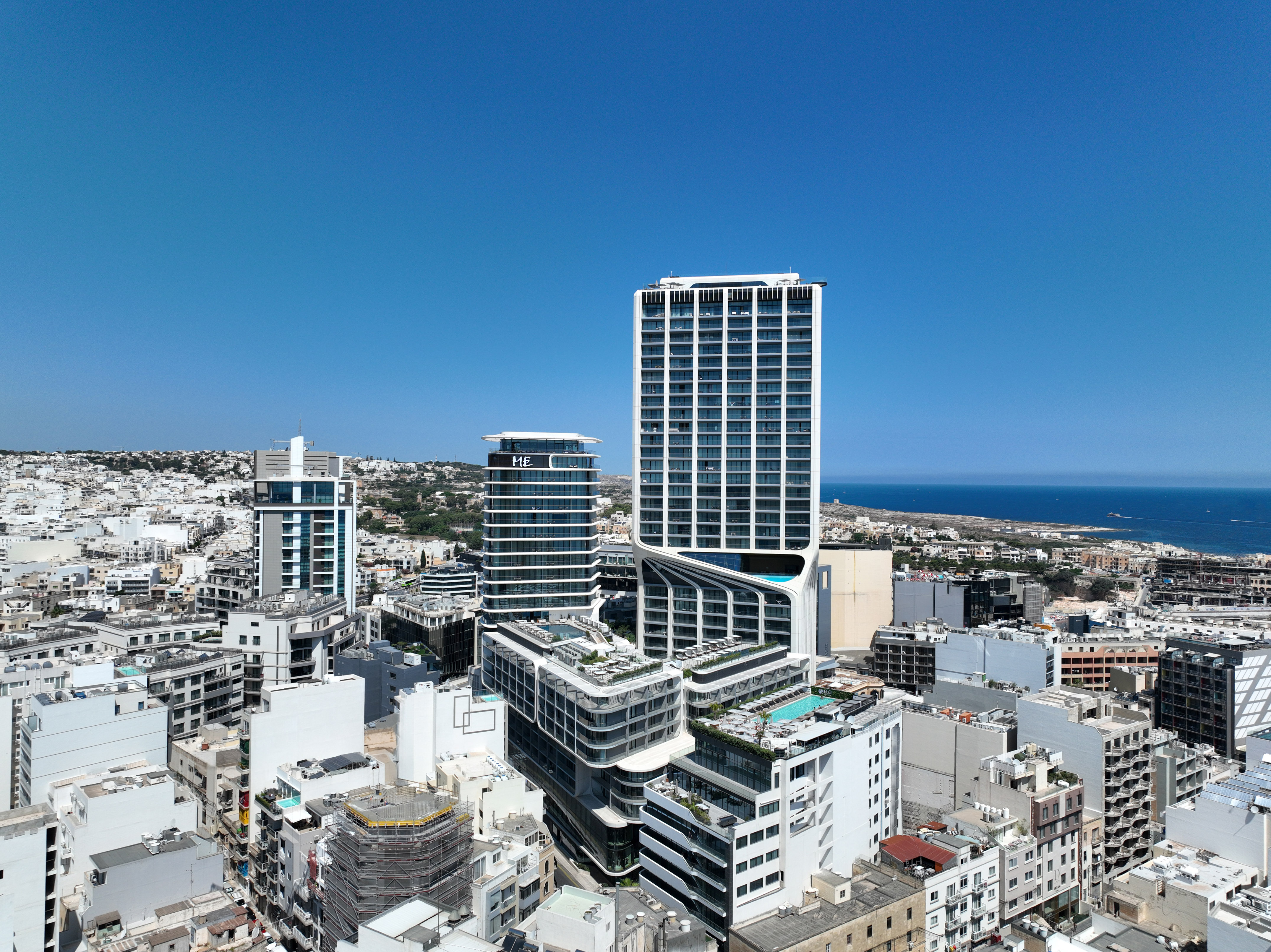 Modern high-rise hotel, rooftop pools, and city skyline with distant sea view.