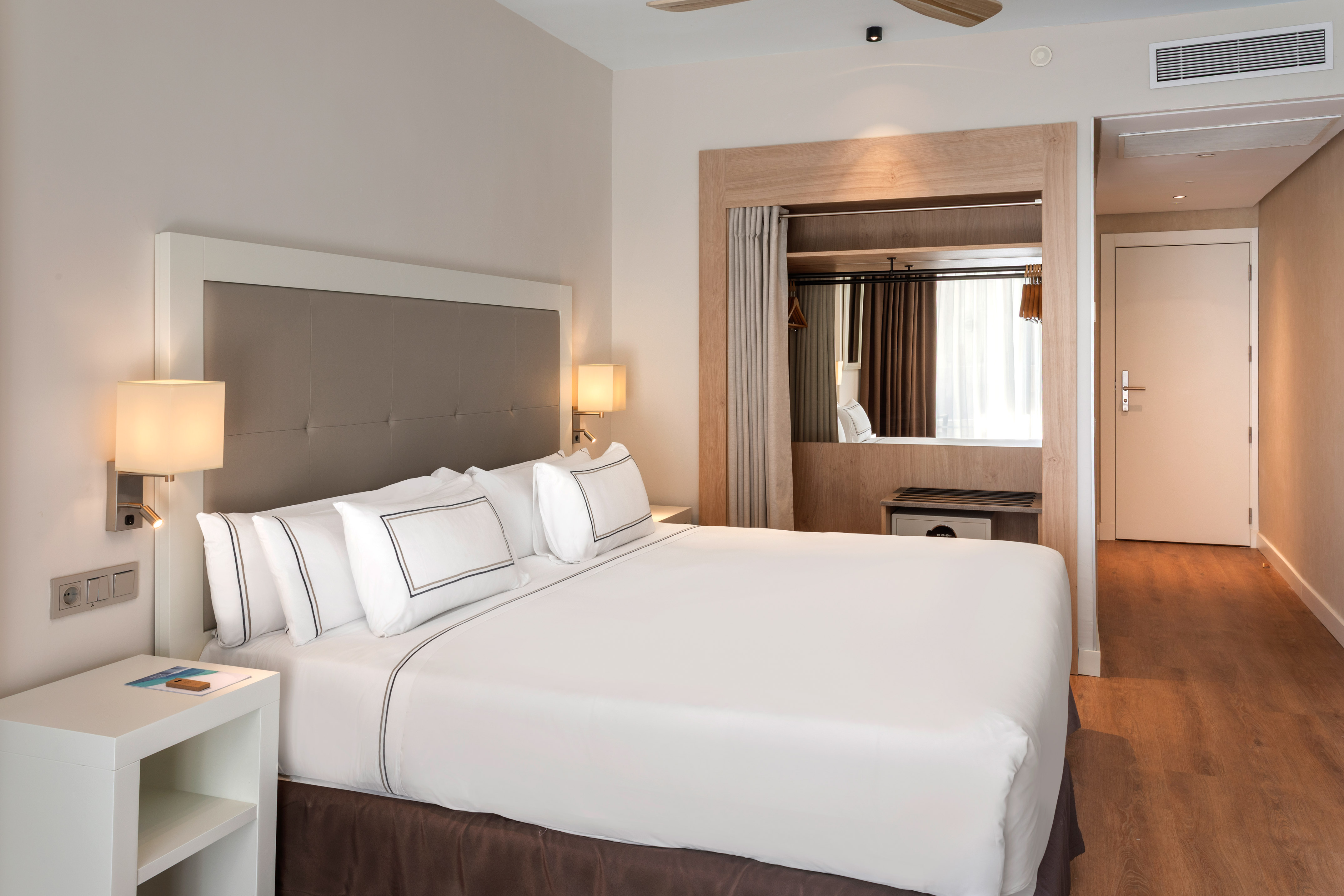 Modern hotel room with a large bed, white linens, and built-in closet.