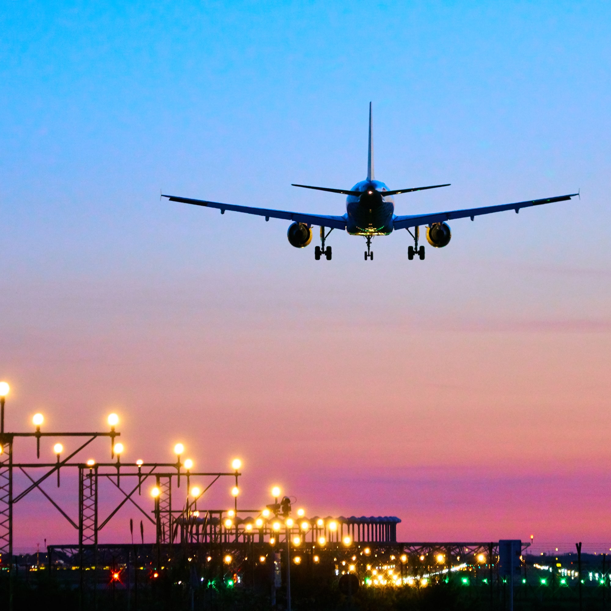 Avión comercial aterrizando sobre aeropuerto iluminado al anochecer.