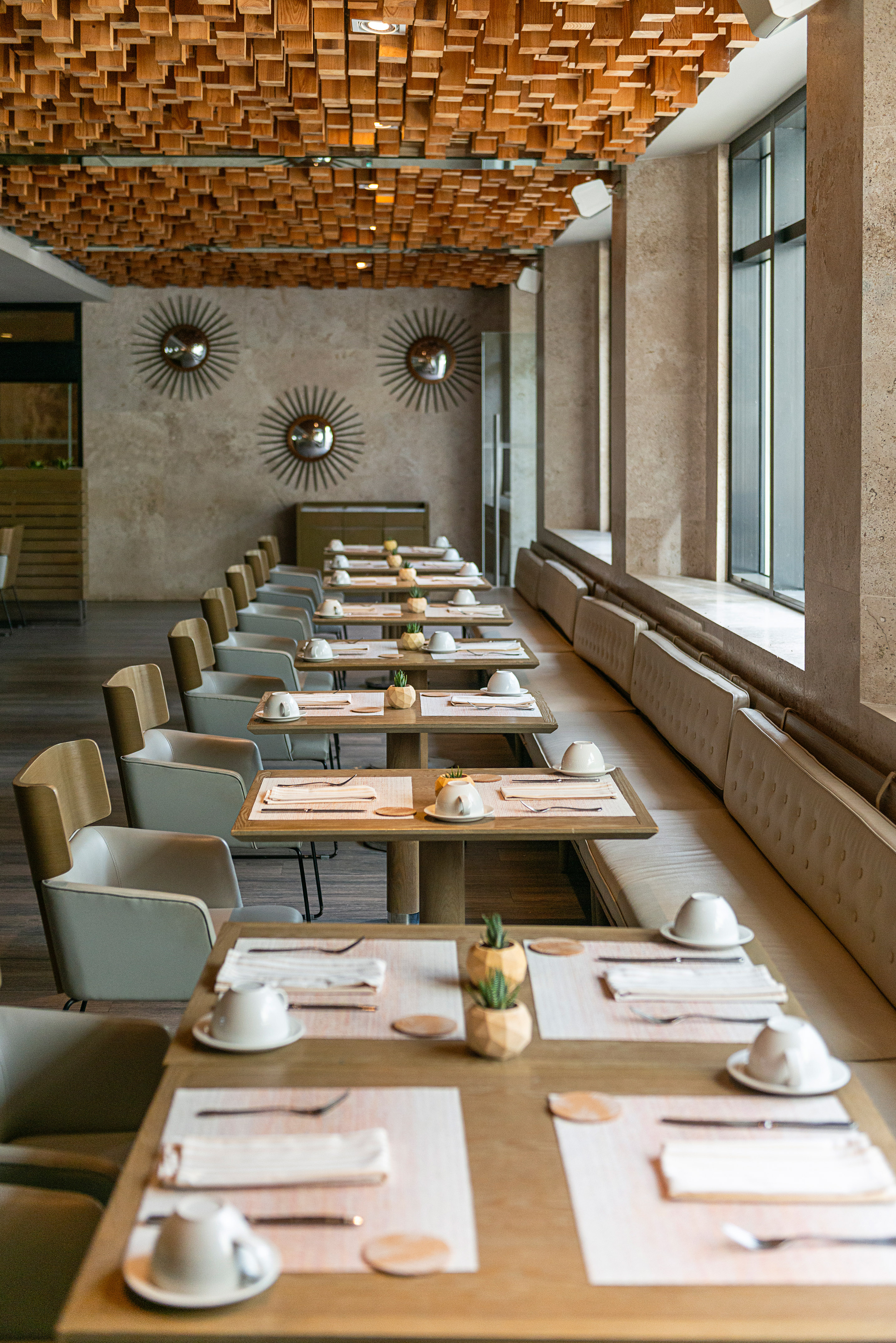 Modern dining room with set tables, wood block ceiling, and window seating.