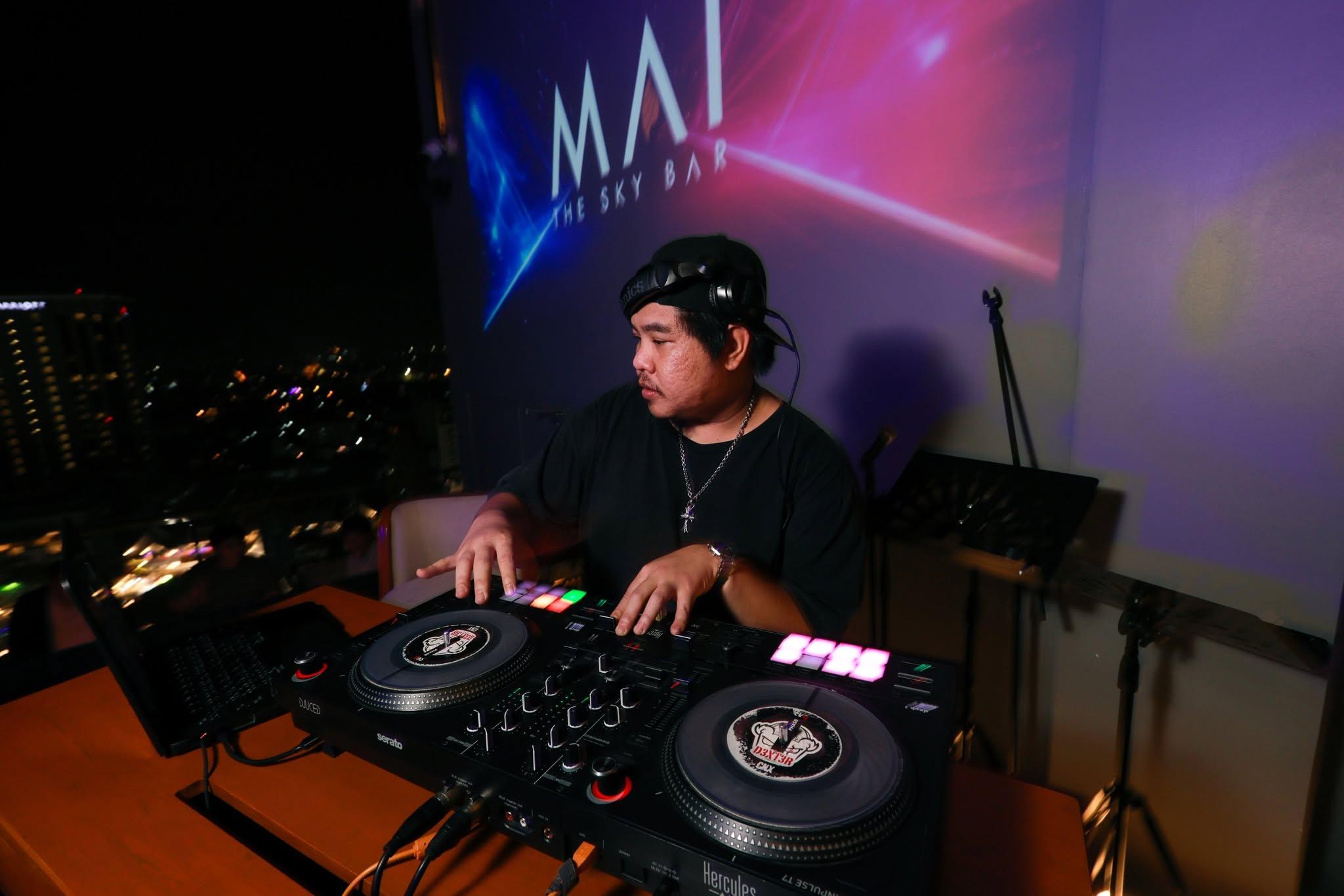 DJ with headphones mixing on controller at a rooftop sky bar at night.