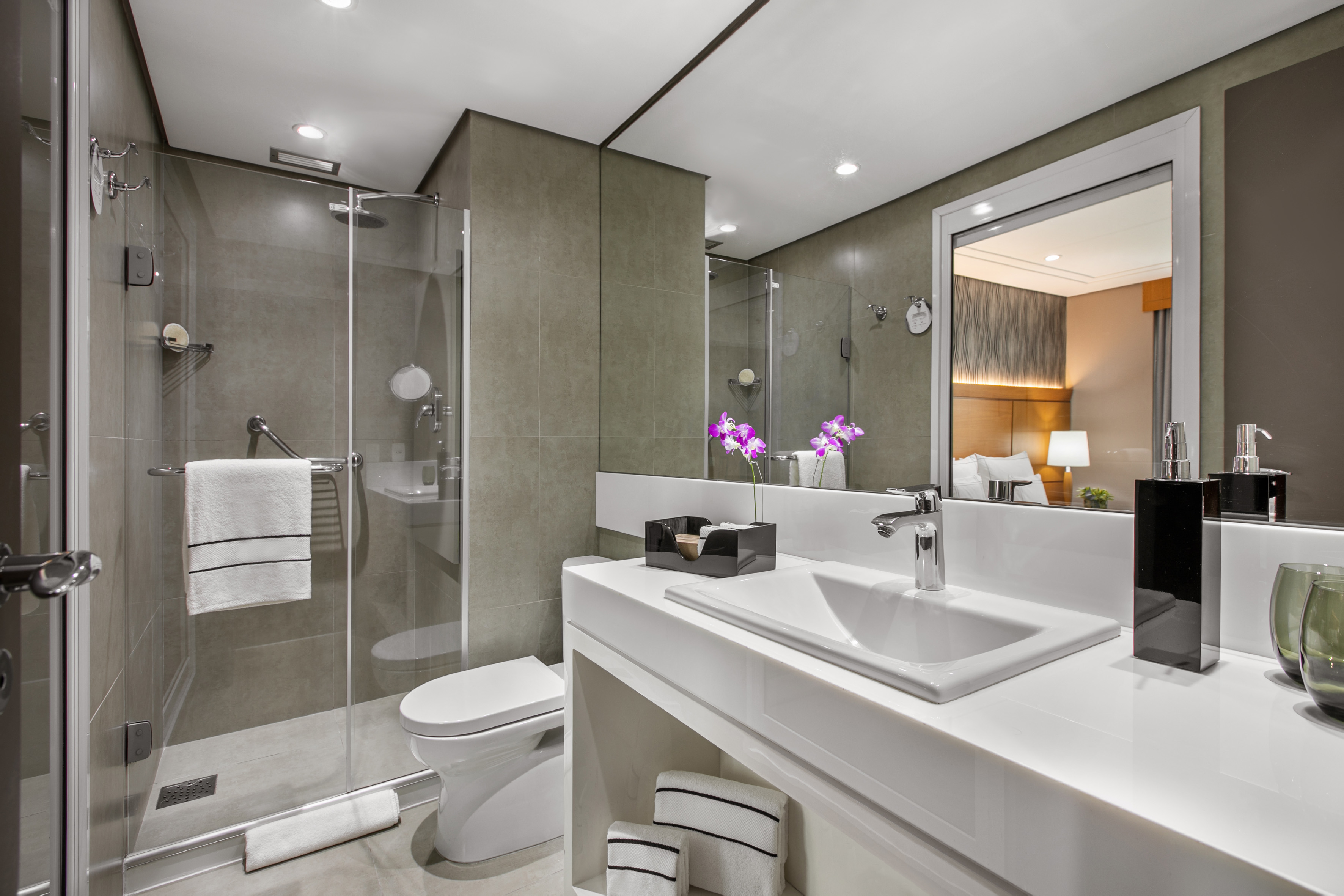 Modern bathroom with walk-in shower, white vanity, and mirrored bedroom view.