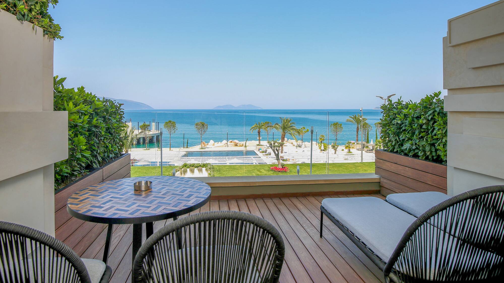 Resort balcony with sea view, wooden deck, outdoor seating, and pool.