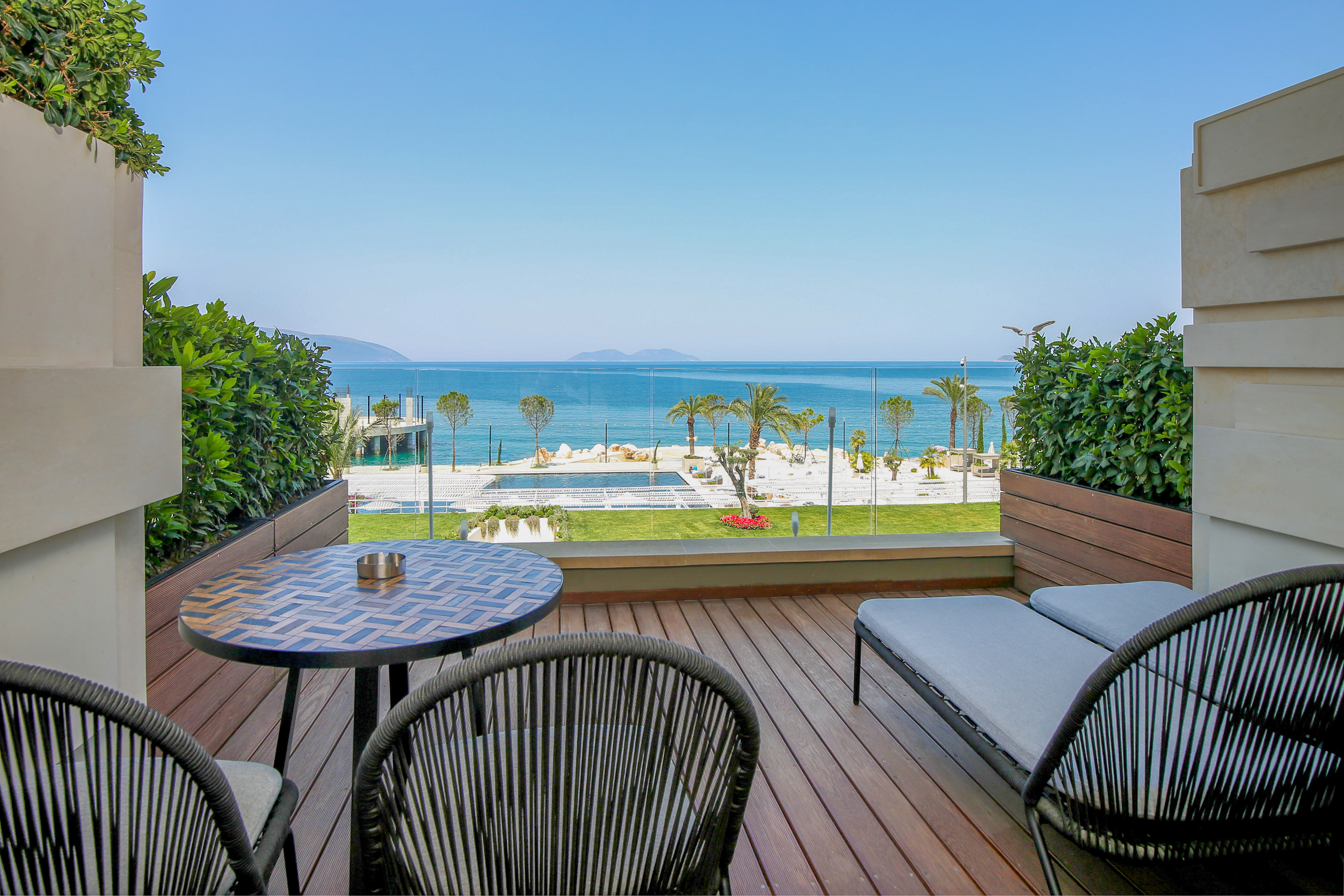 Resort balcony with sea view, wooden deck, outdoor seating, and pool.