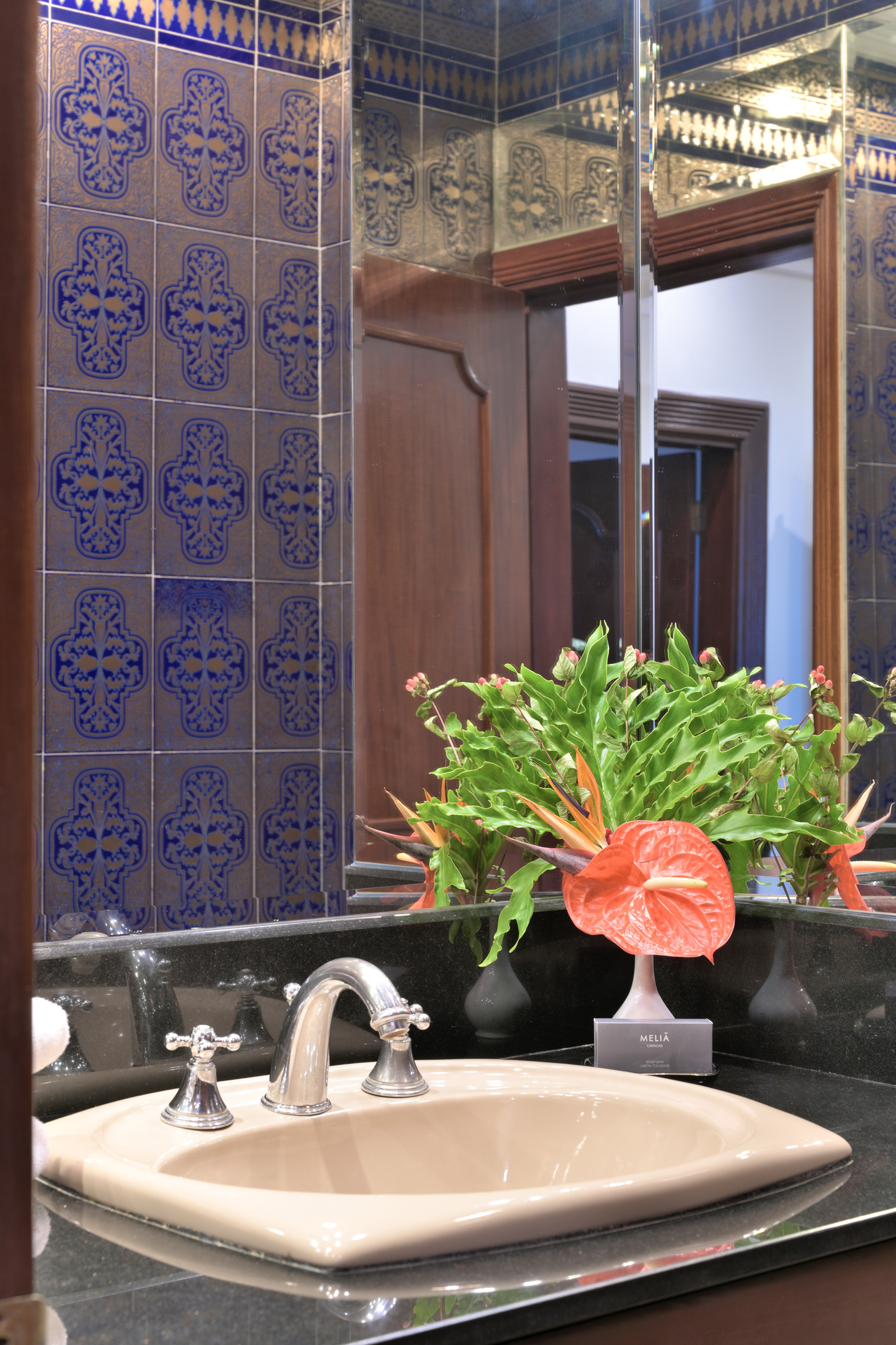 Bathroom vanity with sink, ornate blue and gold tiles, tropical flowers, mirror.