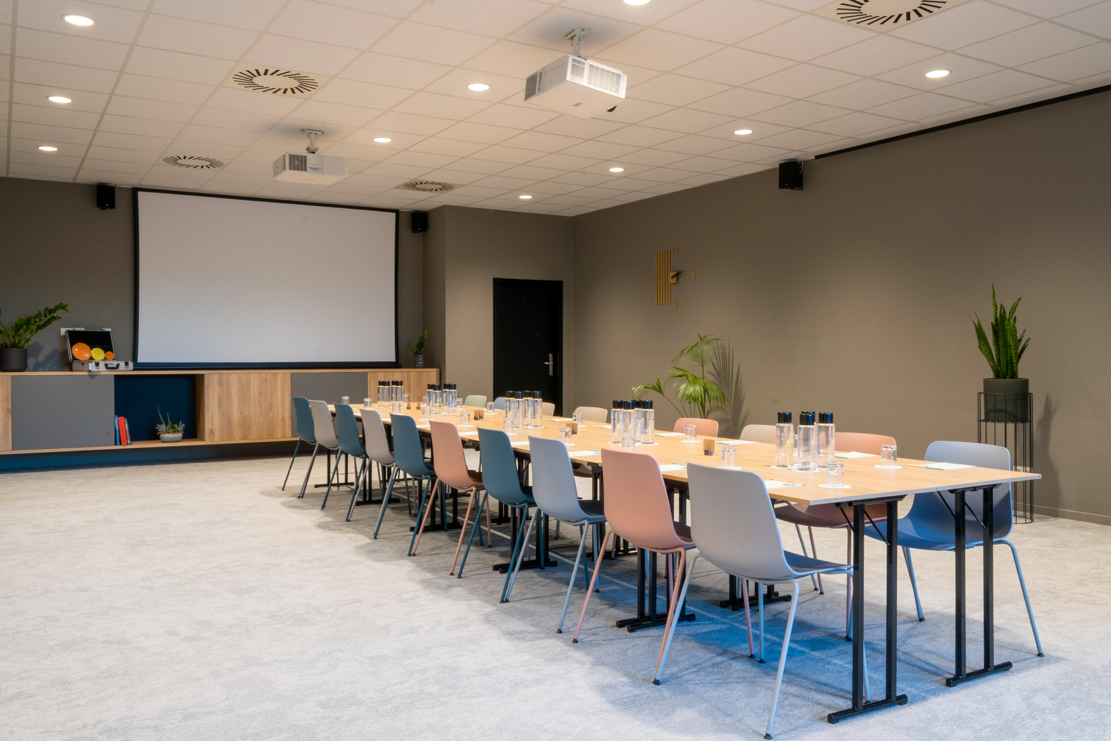Modern conference room with long table, diverse chairs, large screen, and projector.