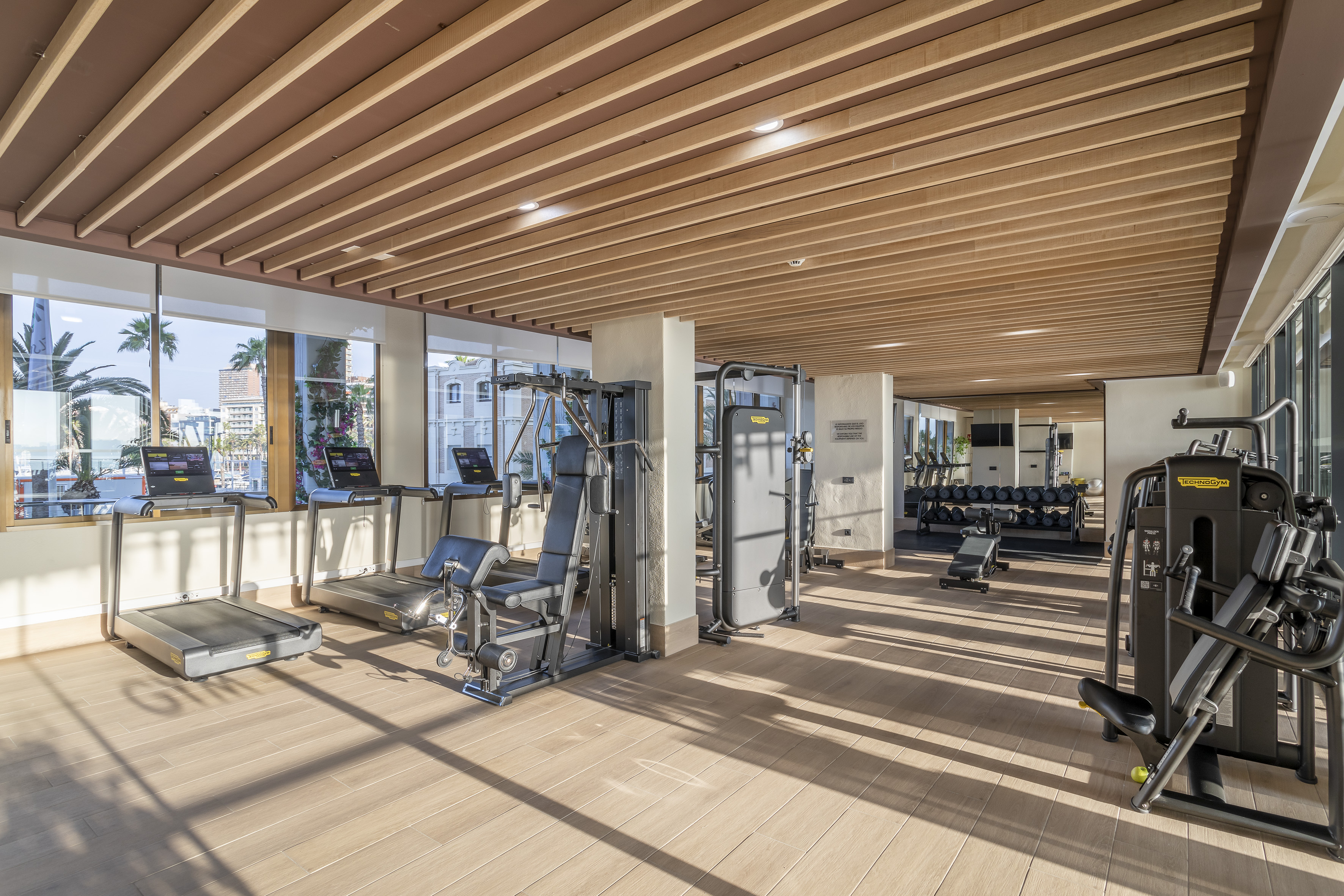 Spacious modern gym with treadmills, weight machines, and dumbbells on wood floor.