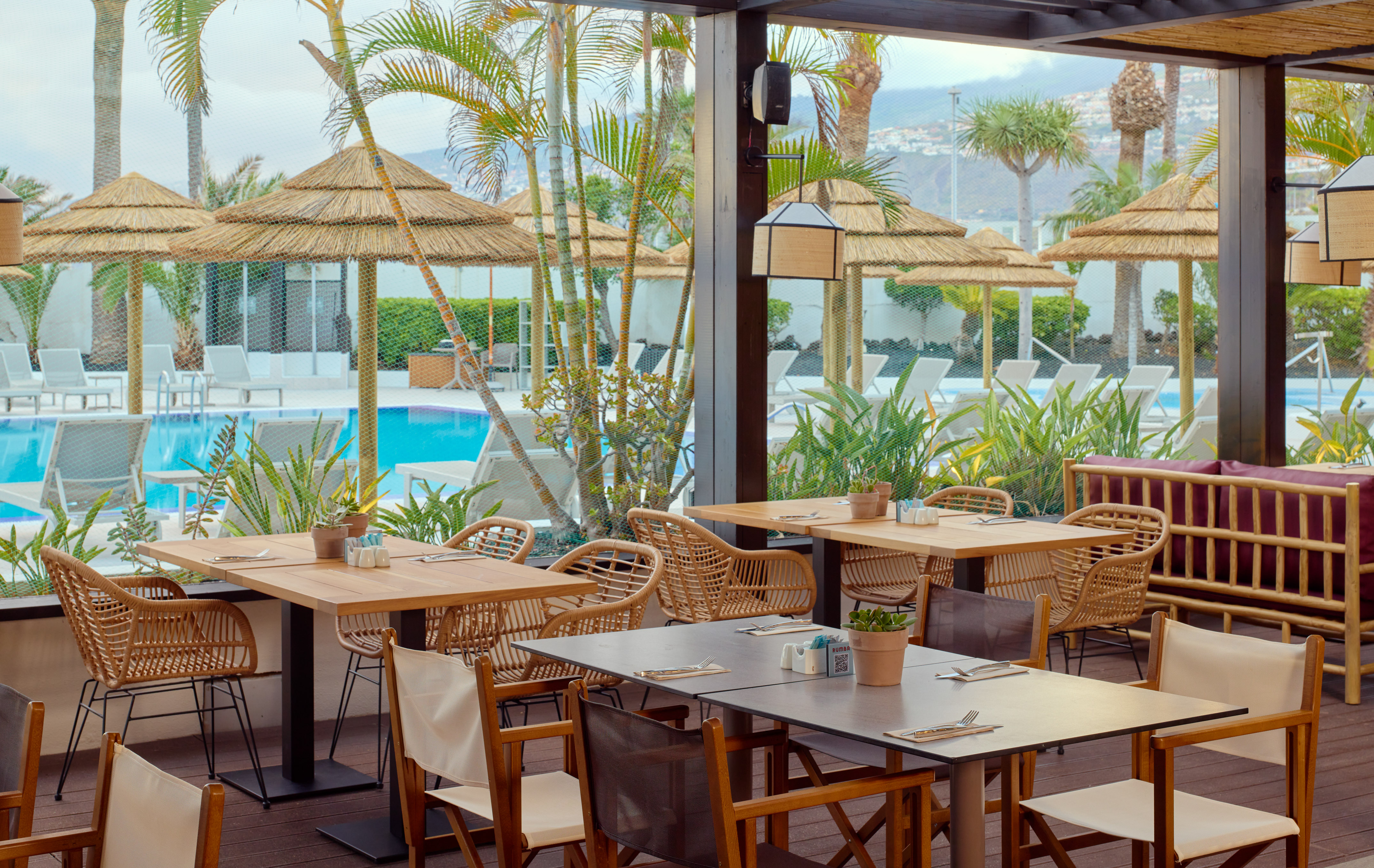 Tropical outdoor restaurant with pool view, palm trees, and rattan furniture.