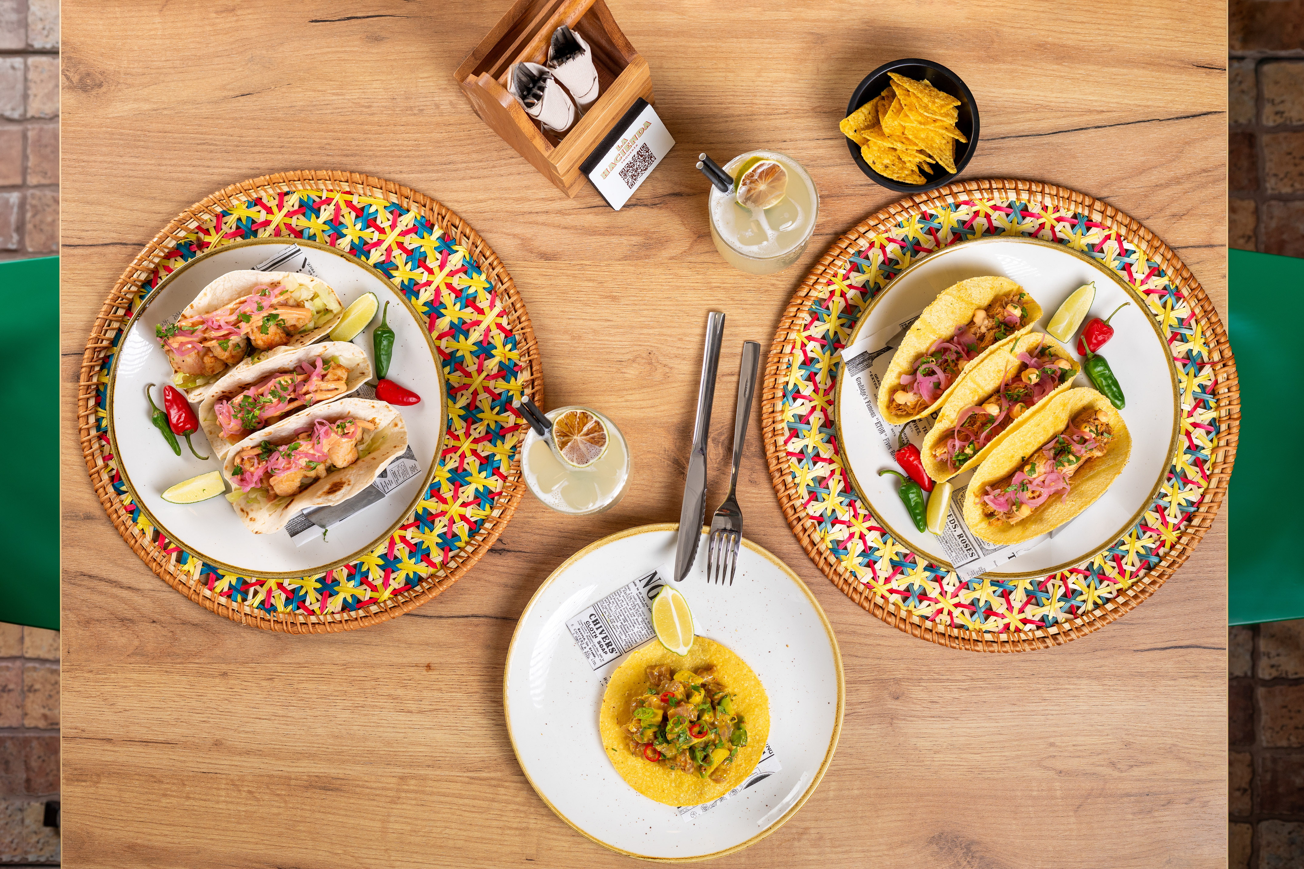 Vibrant Mexican tacos, guacamole, tortilla chips, and cocktails on a wood table.