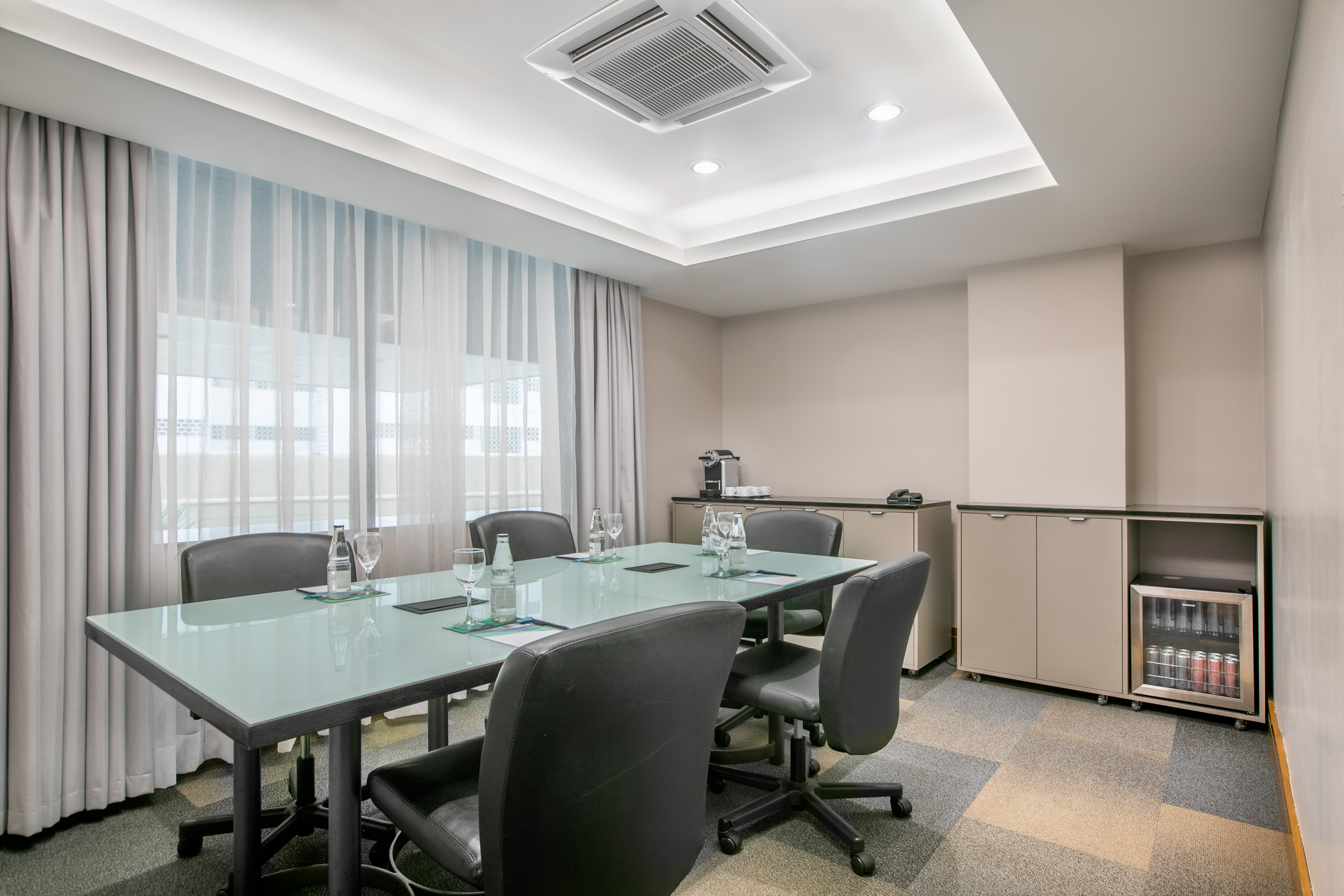 Modern meeting room with glass table, chairs, and refreshments station.