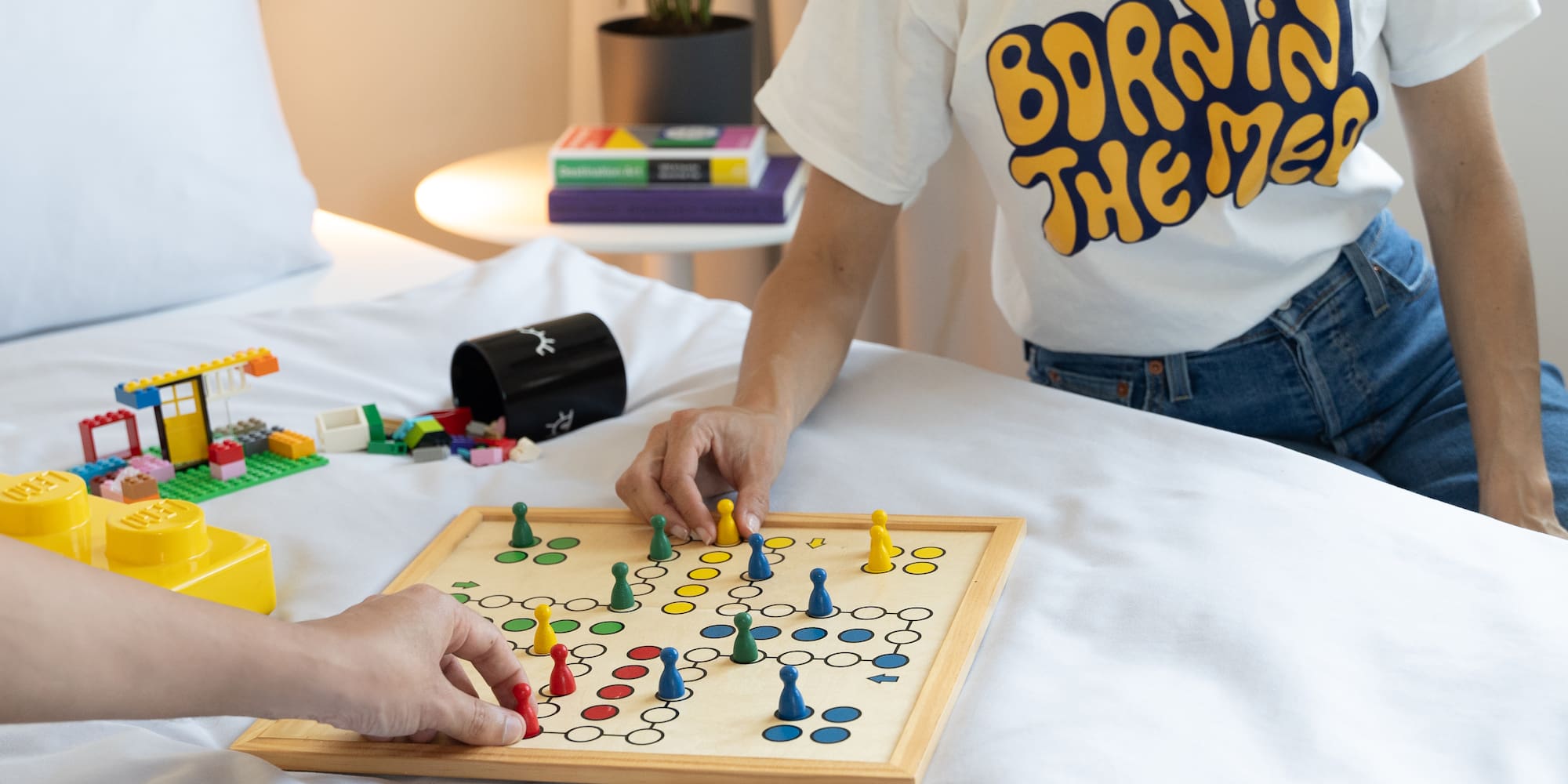 Family playing board game and Lego on white hotel bed.