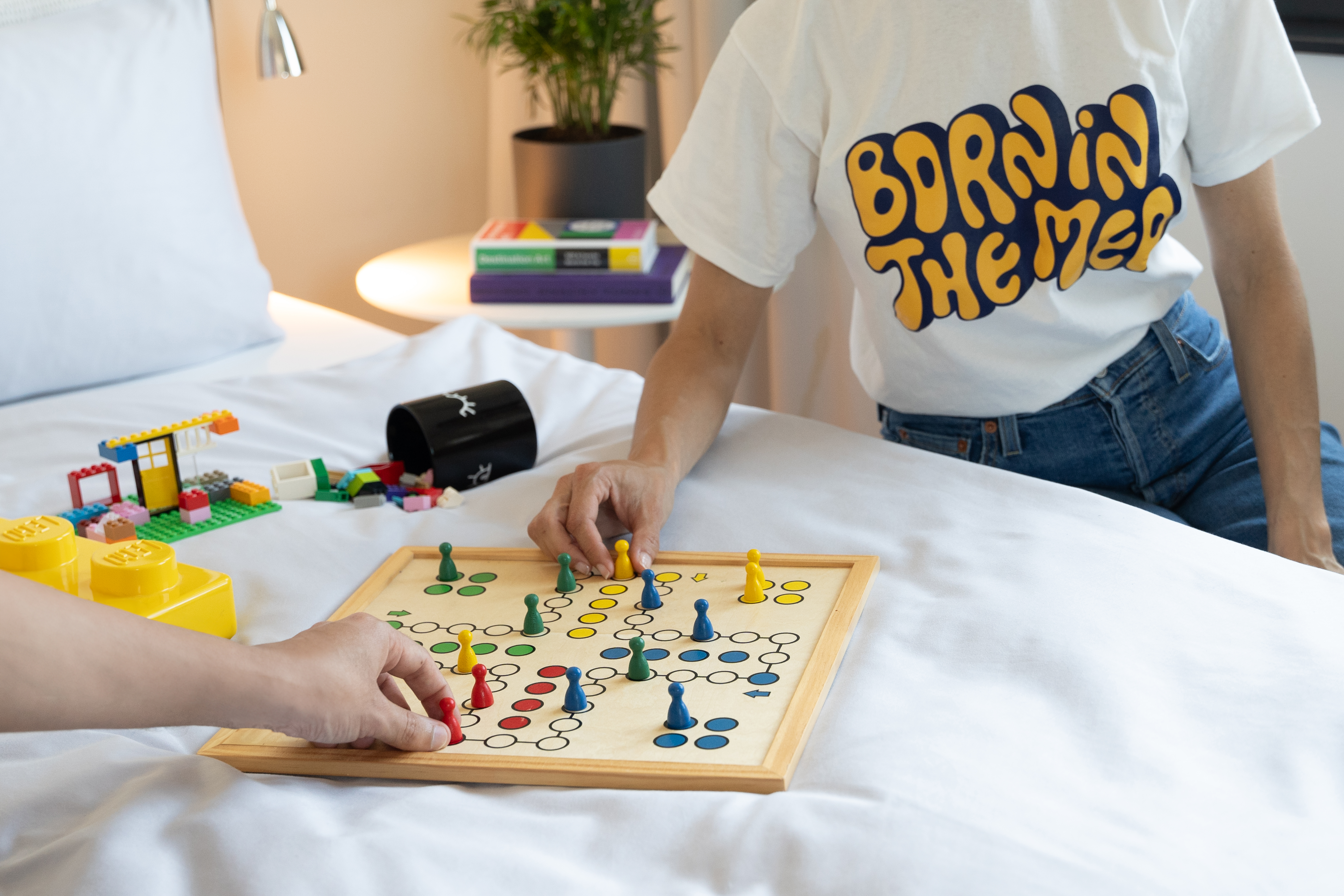 Family playing board game and Lego on white hotel bed.