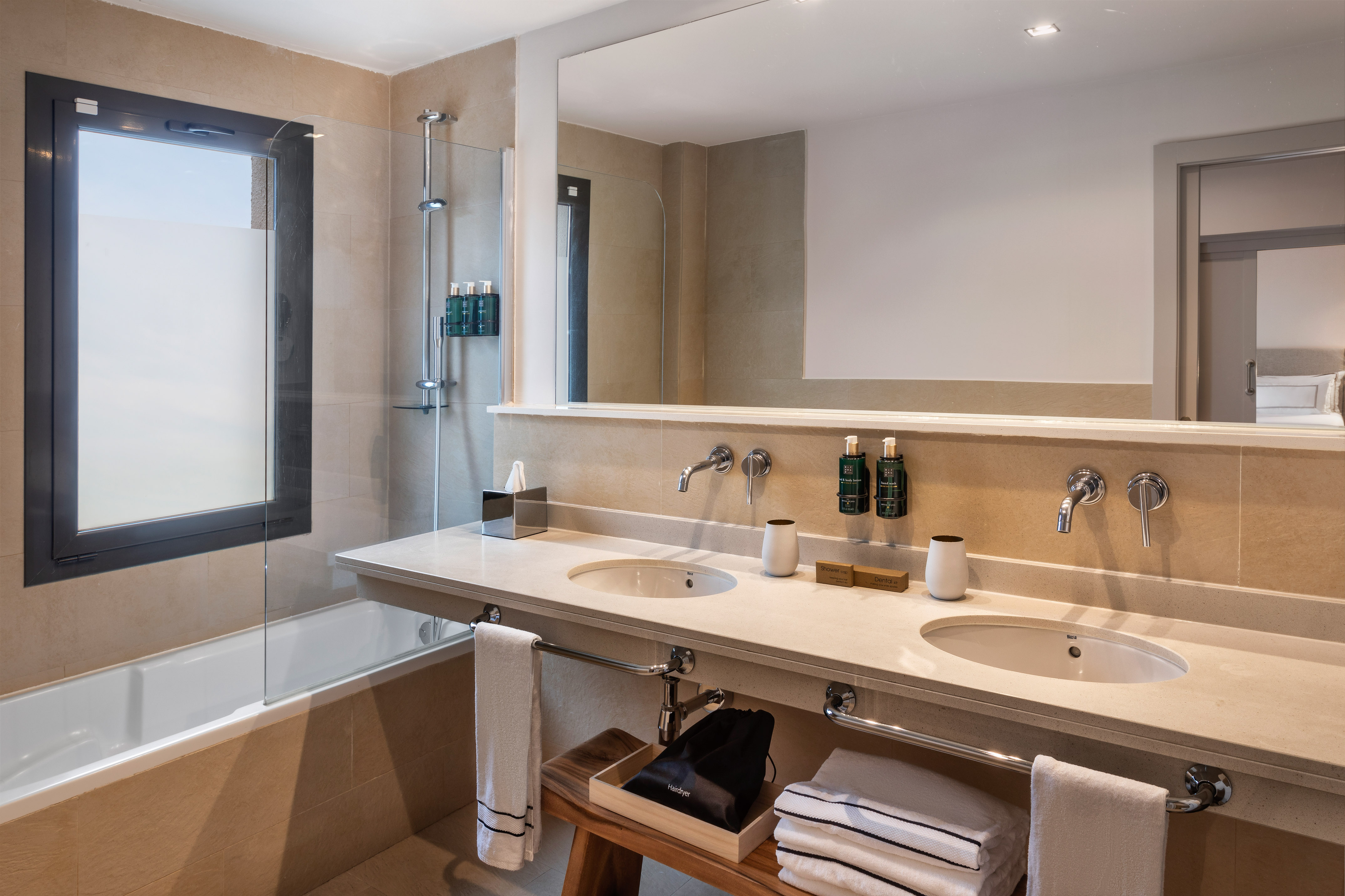 Modern hotel bathroom with double vanity, large mirror, bathtub, and shower.
