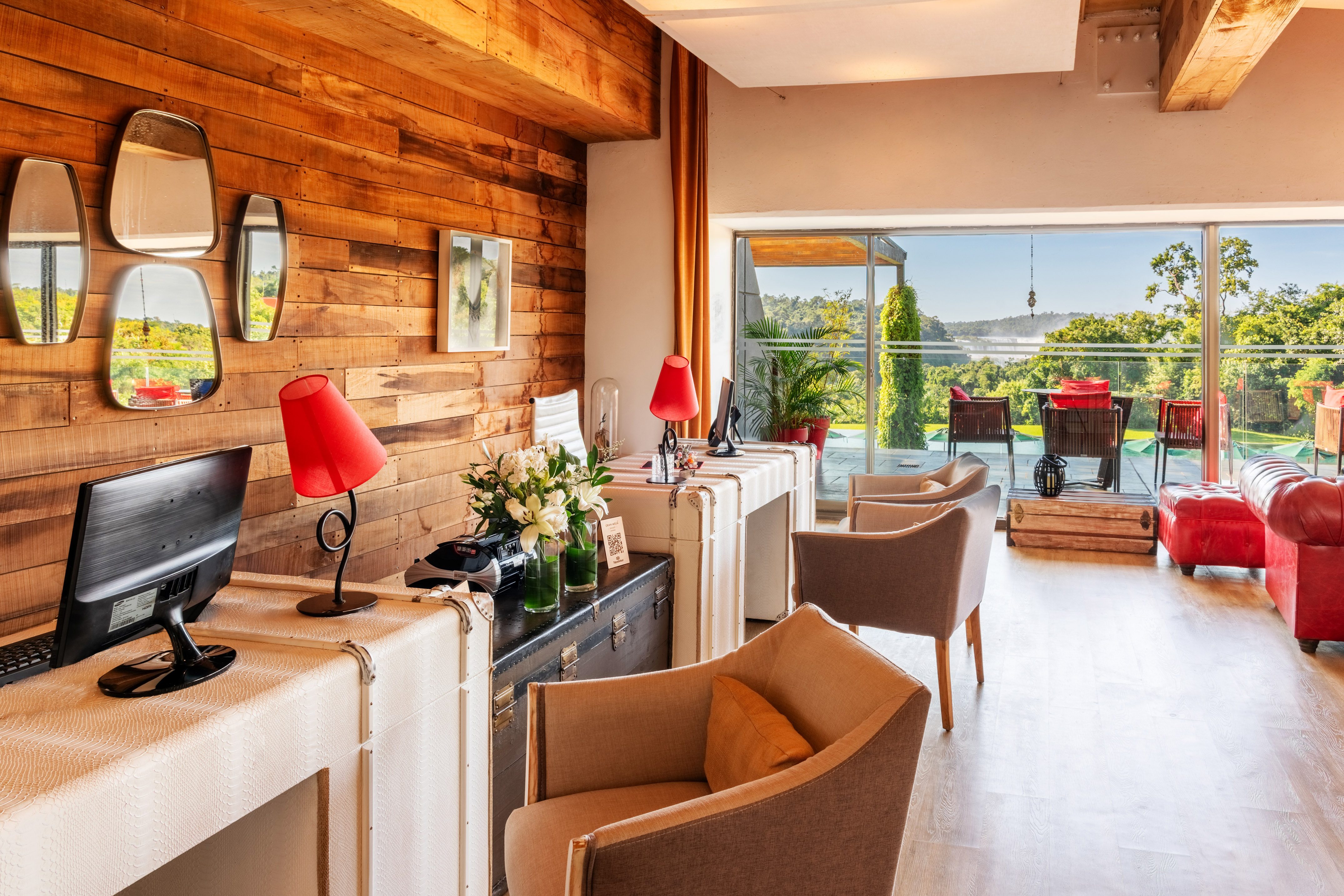 Hotel lobby with wooden wall, desk, cozy seating, and large windows to nature.