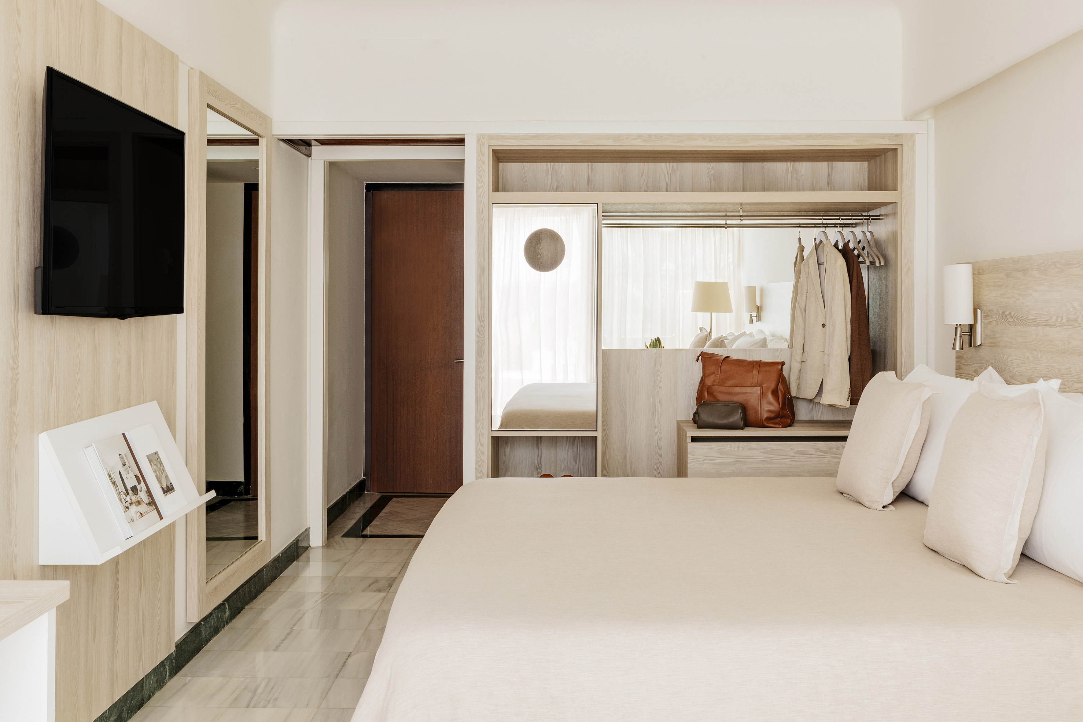 Modern hotel room with light wood, neutral bed, built-in wardrobe and TV.