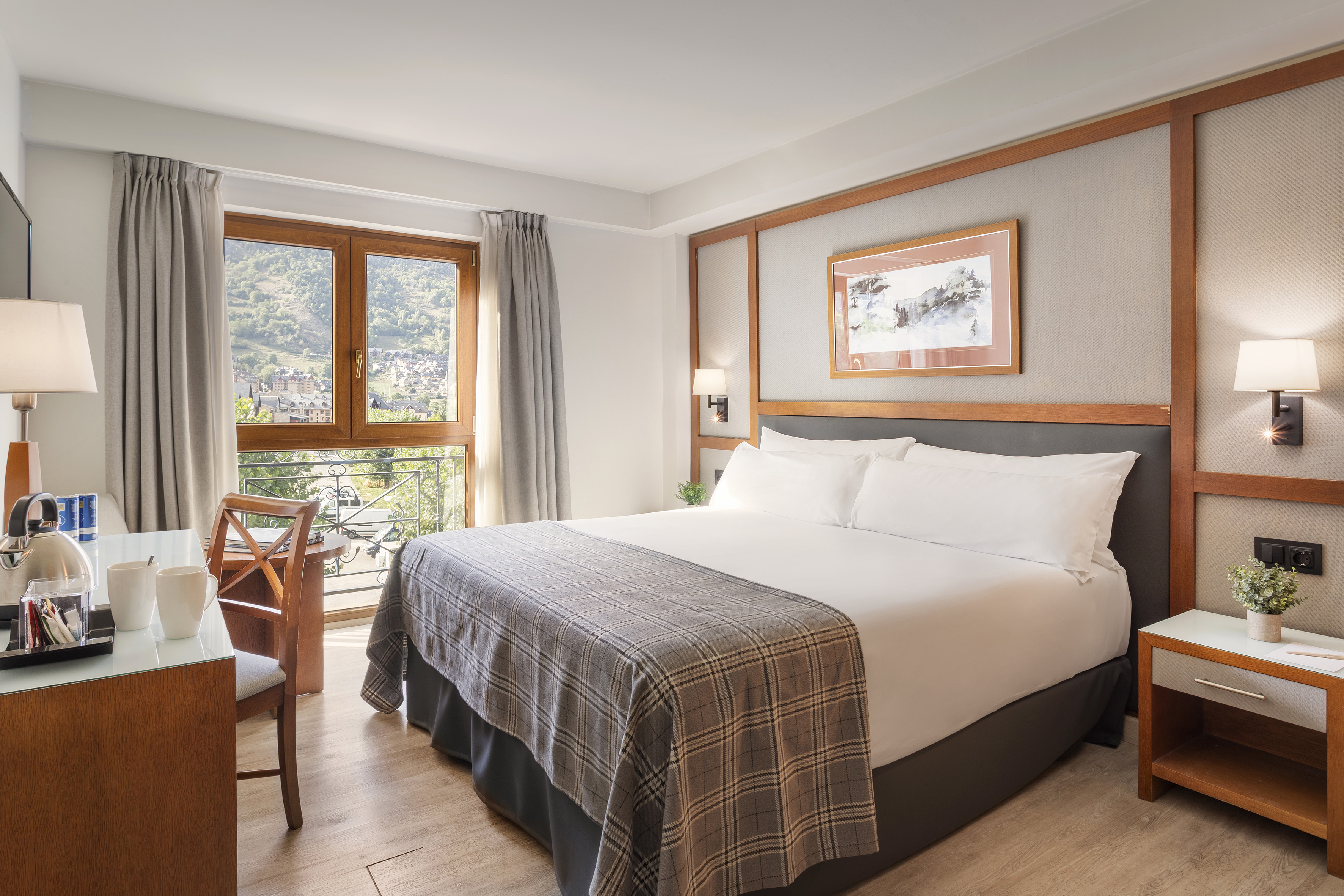 Bright hotel room with large bed, mountain view balcony, and coffee setup.