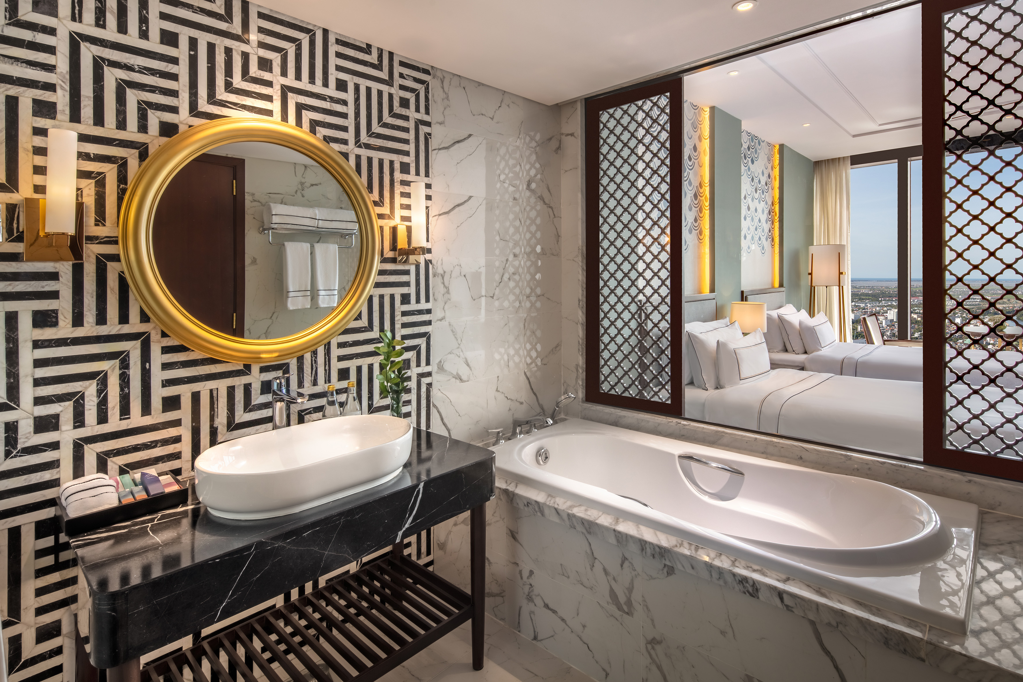 Luxury hotel bathroom: geometric wall, gold mirror, marble, bathtub, and city view.