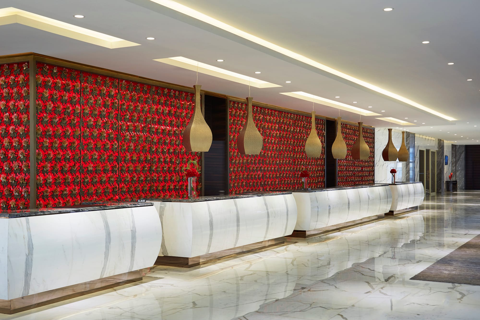 Hotel reception: marble counters, red floral wall, modern pendant lights.