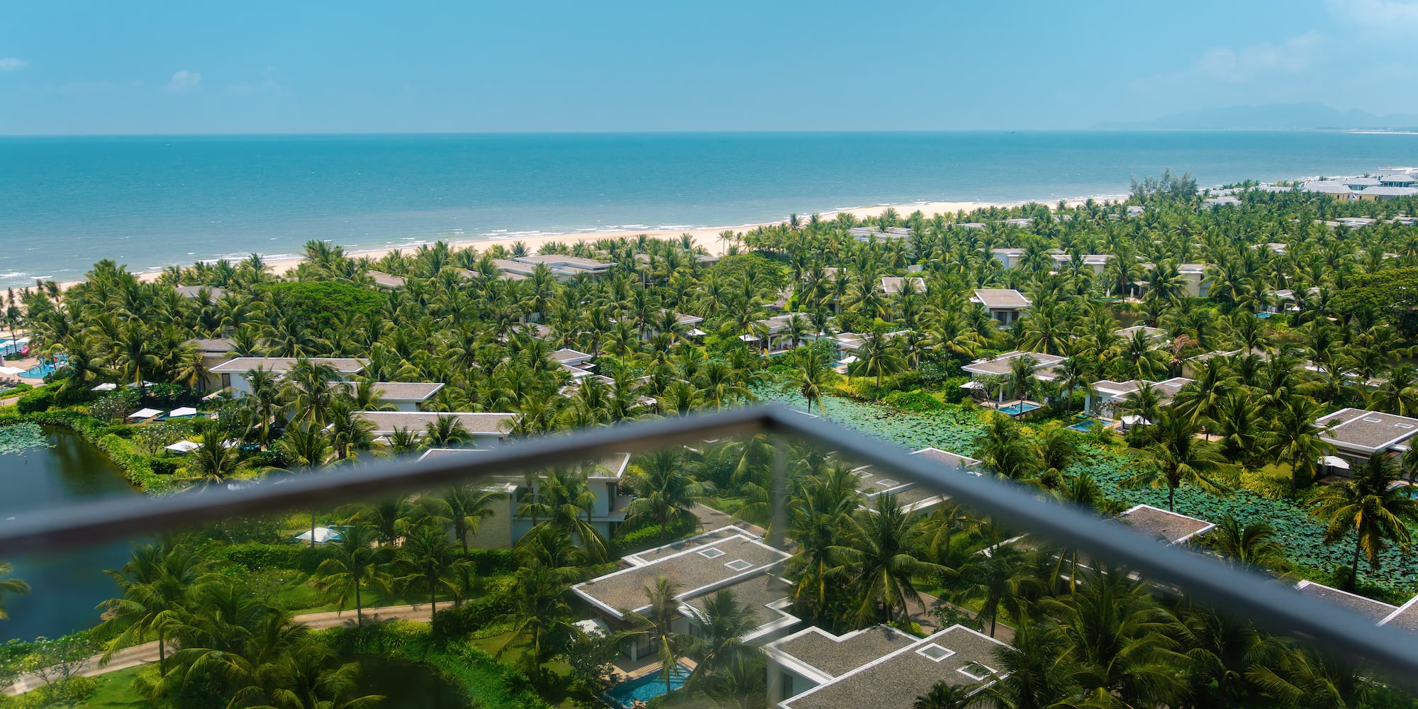 High view of tropical resort villas, palm trees, sandy beach, and blue ocean.