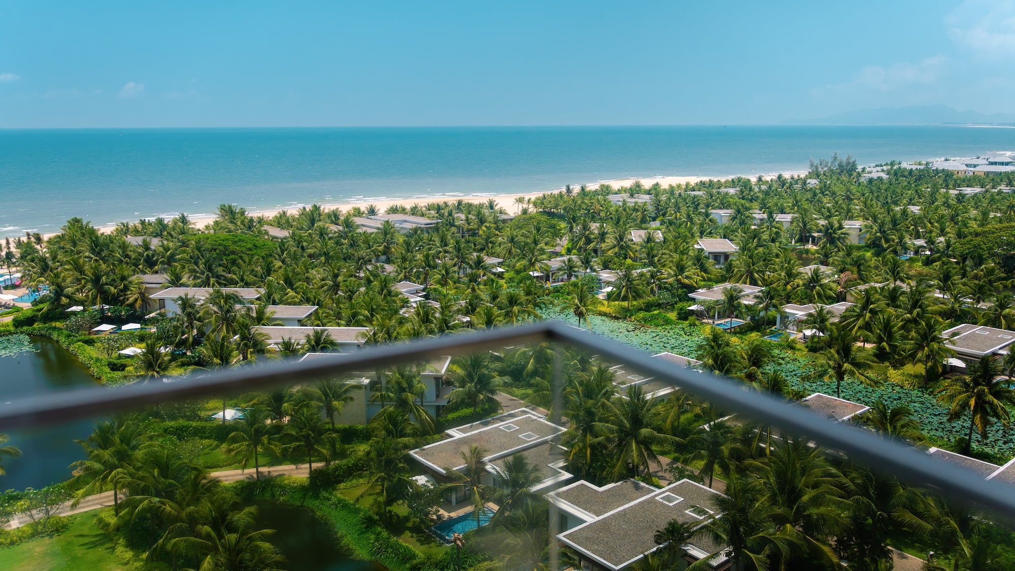 High view of tropical resort villas, palm trees, sandy beach, and blue ocean.