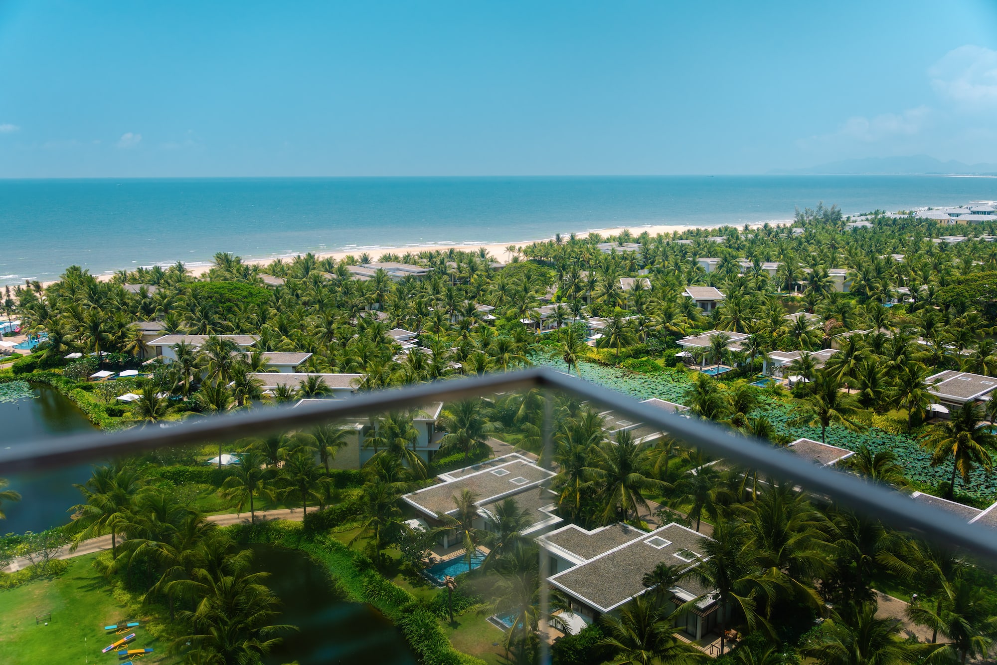High view of tropical resort villas, palm trees, sandy beach, and blue ocean.