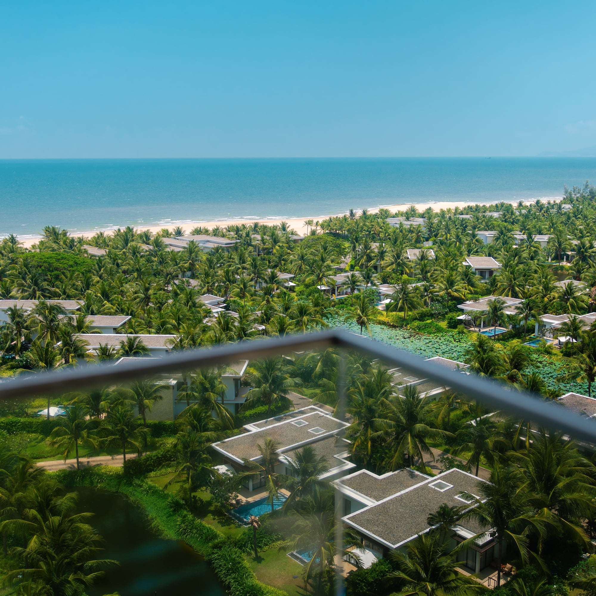 High view of tropical resort villas, palm trees, sandy beach, and blue ocean.