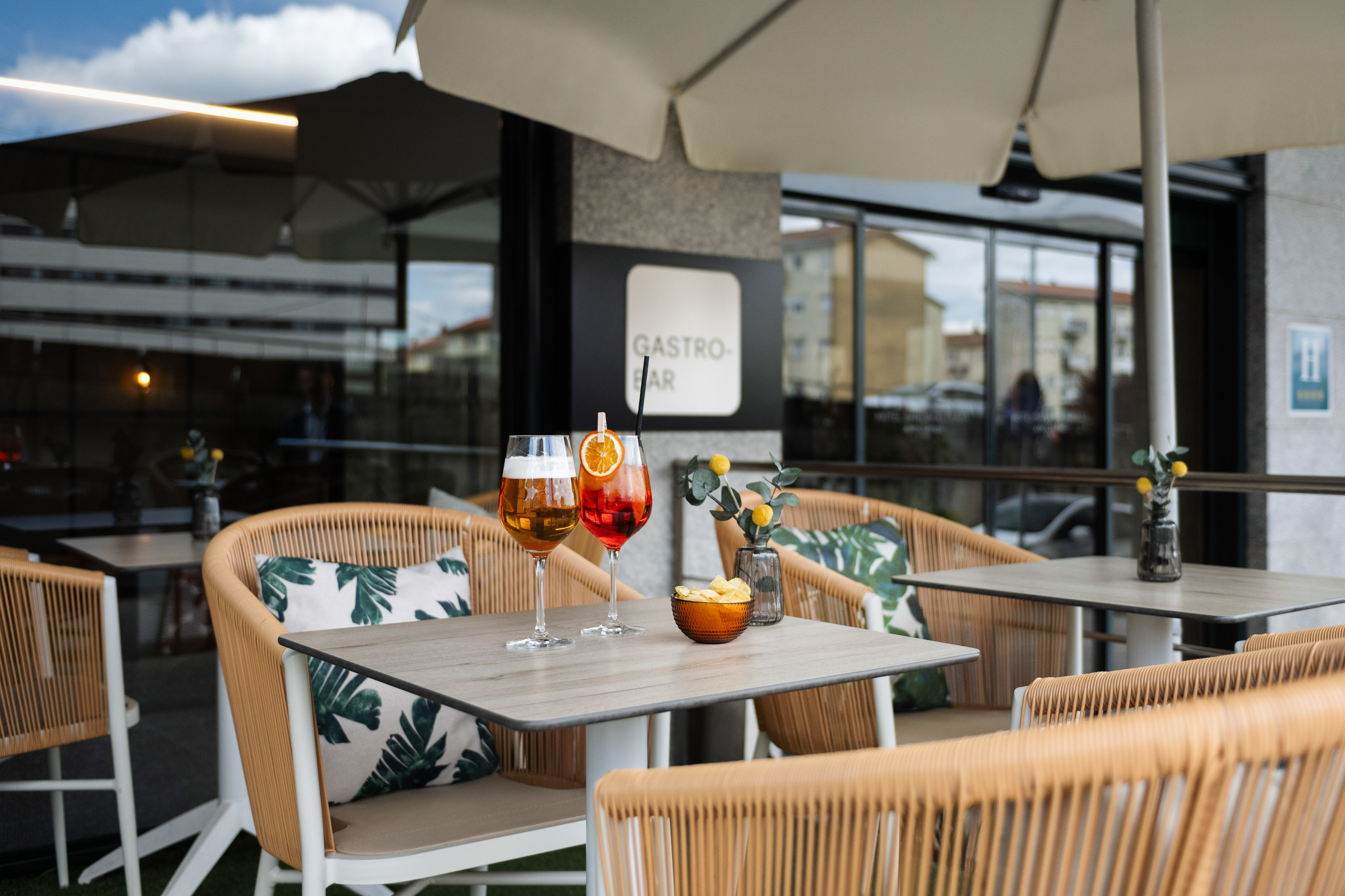 Outdoor gastro bar patio with beer, orange cocktail, chips, and wicker seating.