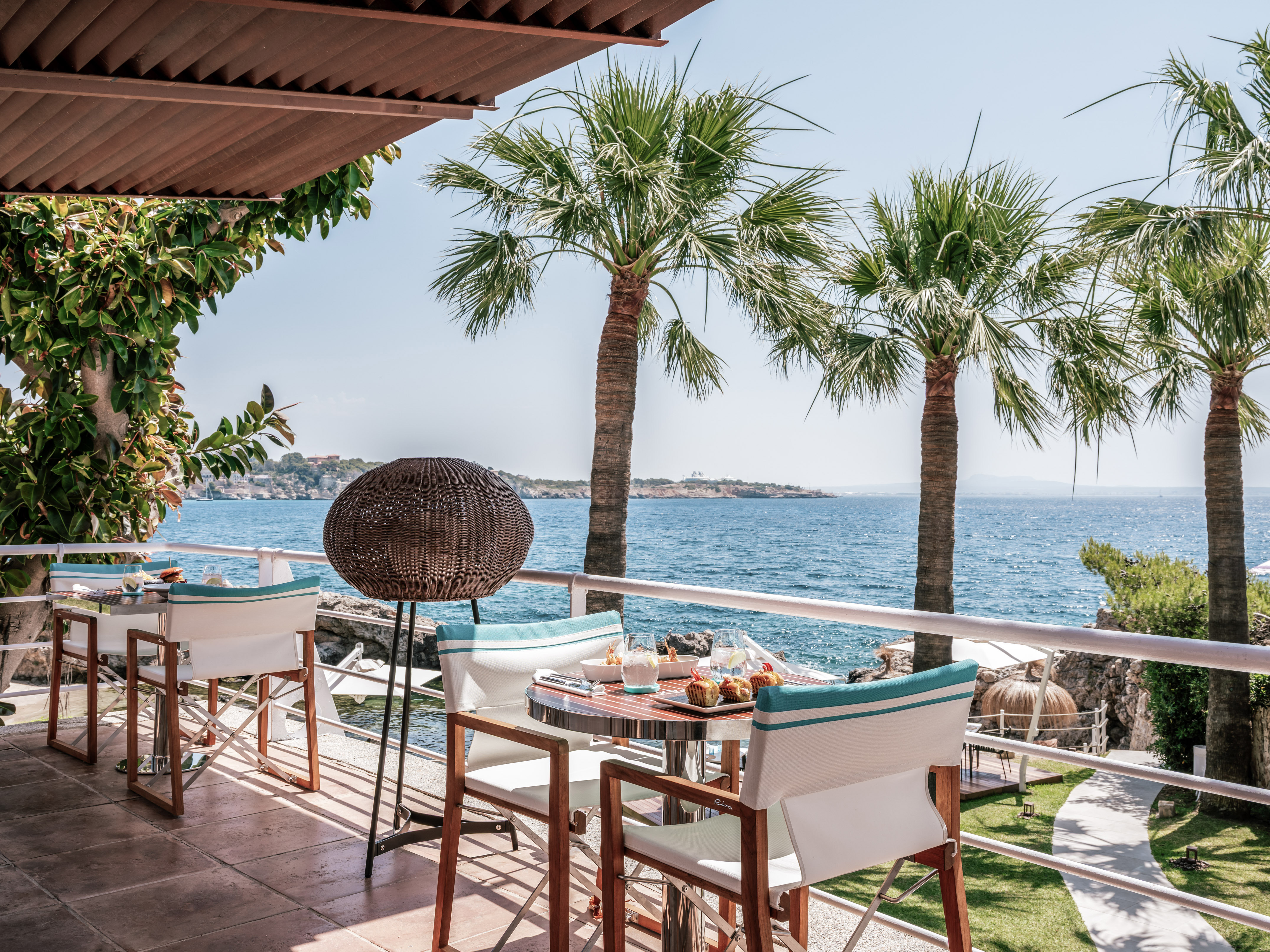 Breakfast on oceanfront terrace with palm trees and blue Mediterranean sea.
