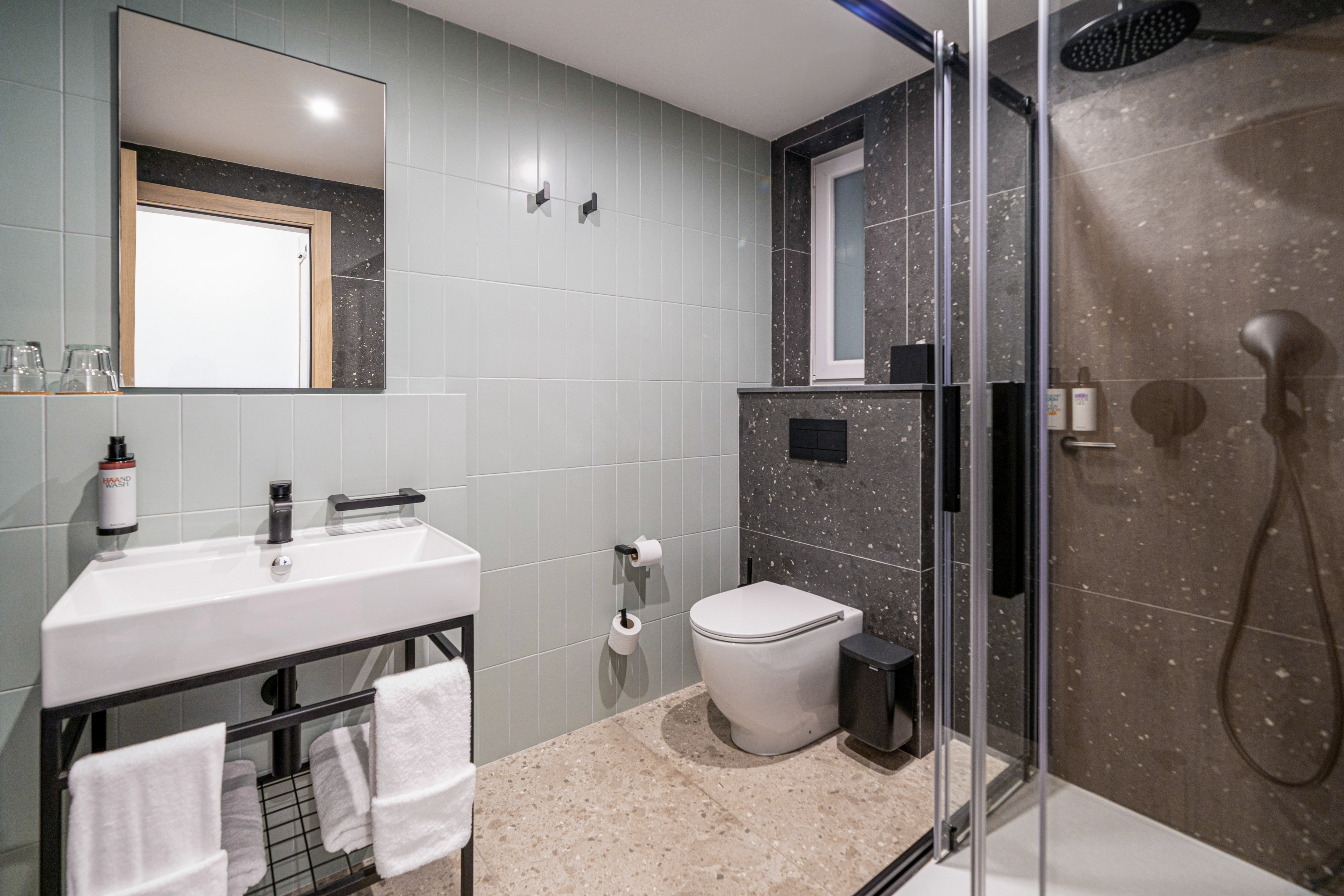 Modern hotel bathroom with mint green and dark speckled tiles, shower, sink, and toilet.