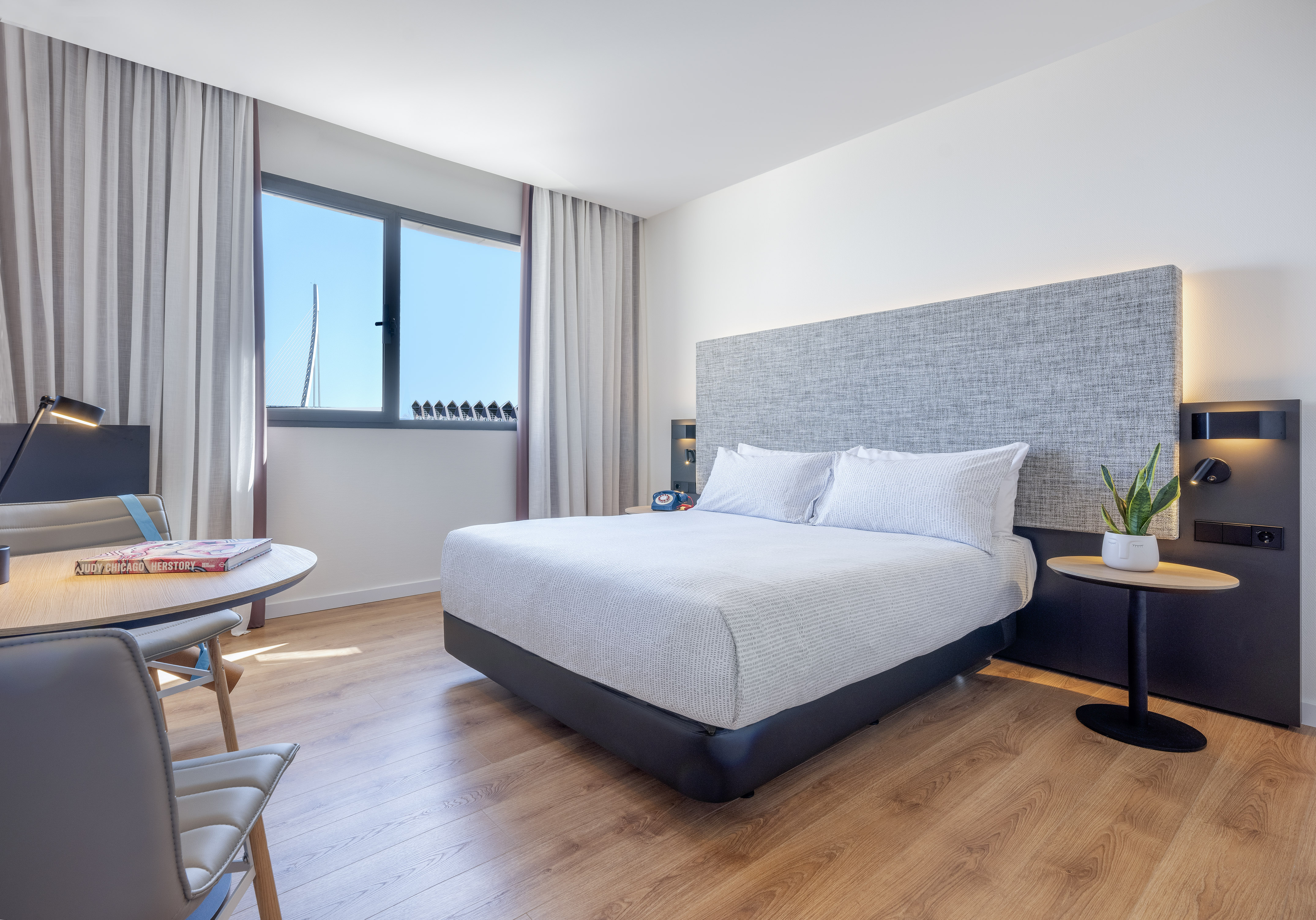 Modern hotel room with bed, desk, and window showing a bridge.