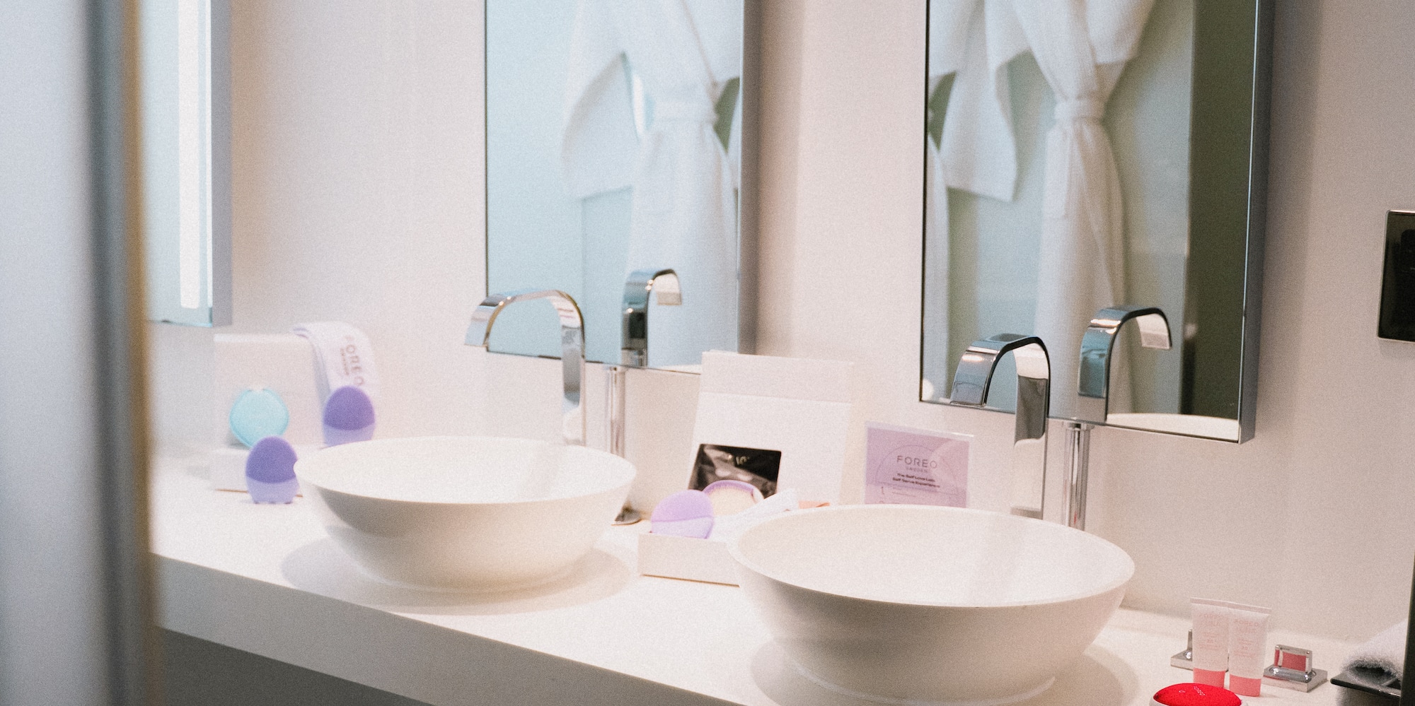 Sleek double bathroom vanity with white vessel sinks, mirrors reflecting bathrobes.