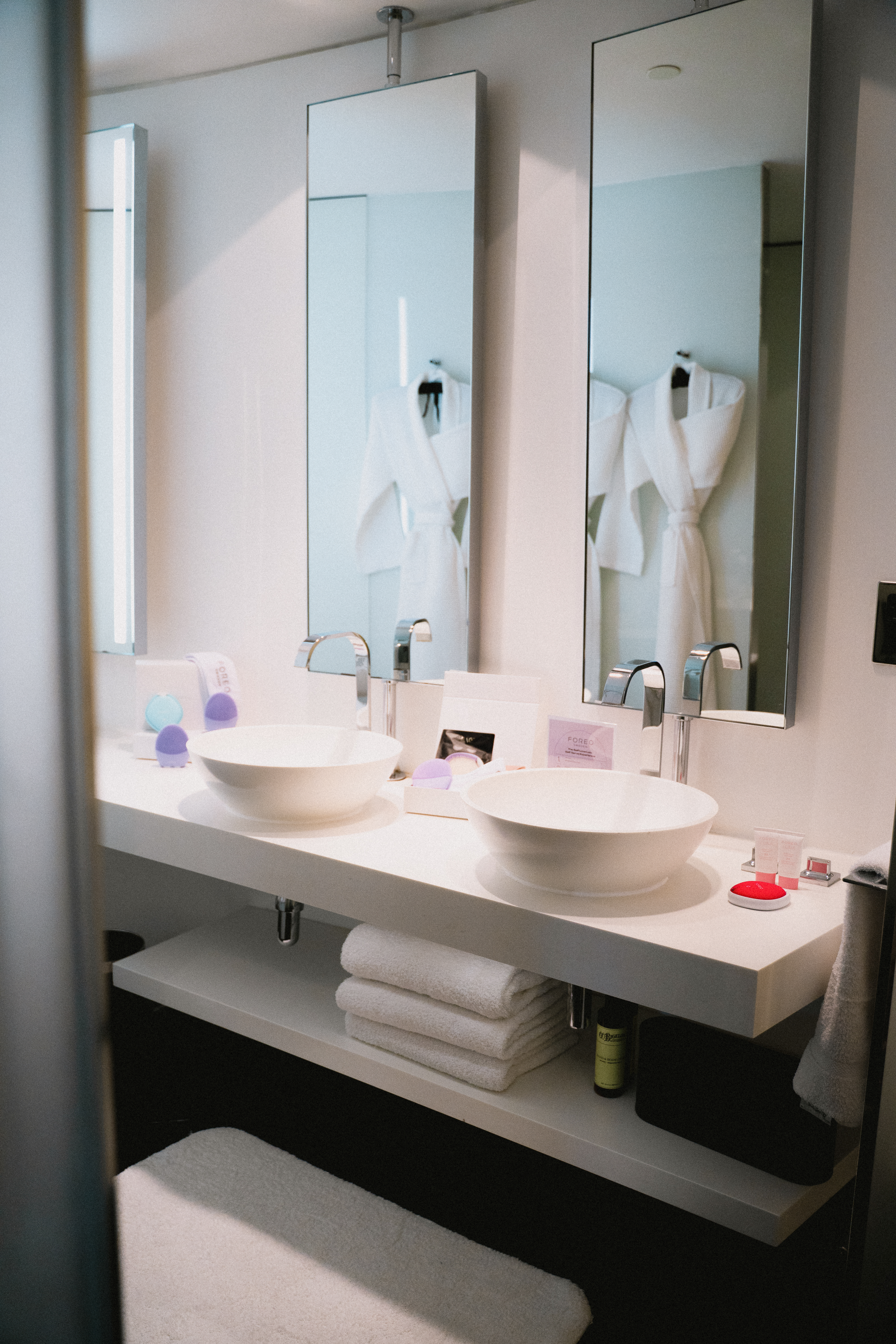Sleek double bathroom vanity with white vessel sinks, mirrors reflecting bathrobes.