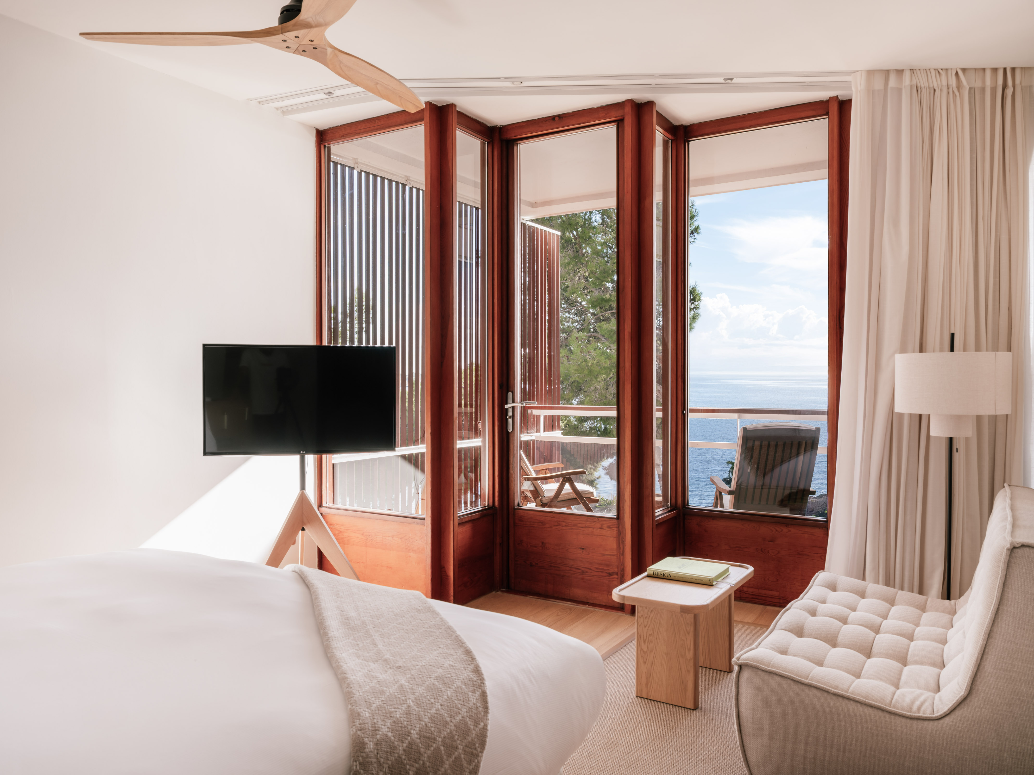 Bedroom with ocean view, balcony, wooden-framed doors, and ceiling fan.