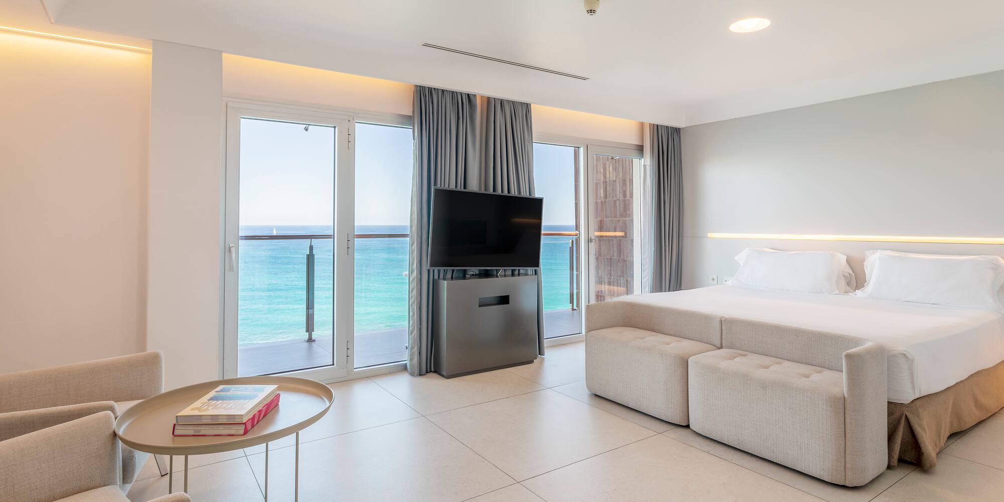 Luxury hotel room with ocean view balcony, large bed, and TV.