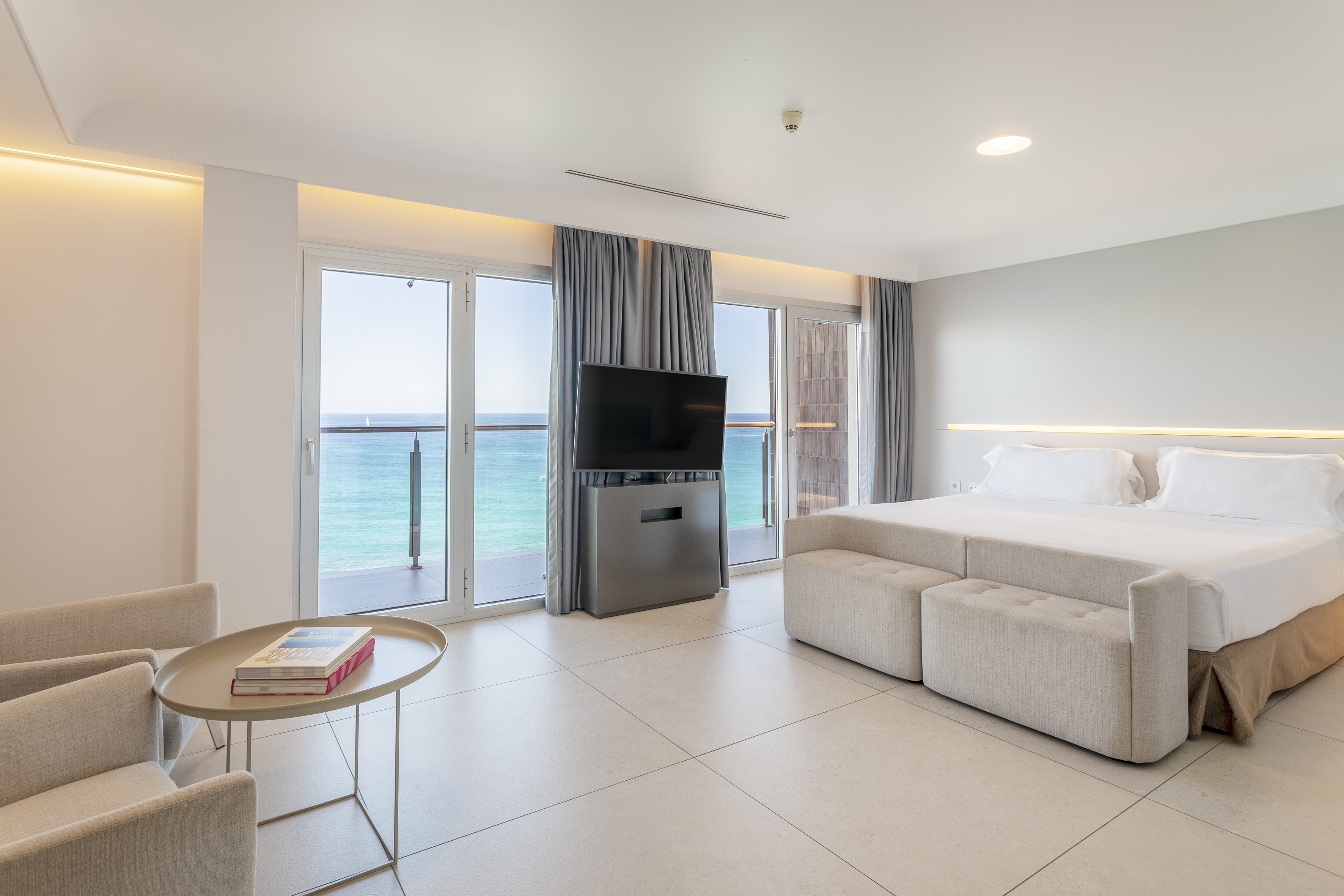 Luxury hotel room with ocean view balcony, large bed, and TV.