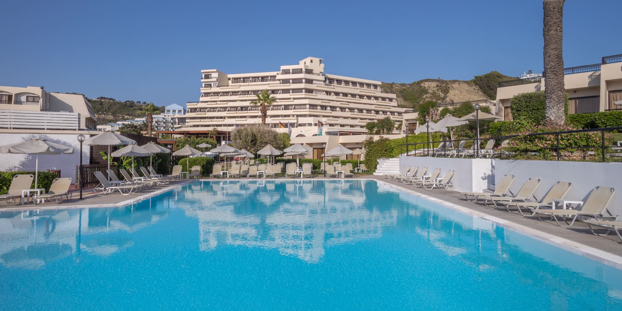 Resort hotel with large outdoor swimming pool, sun loungers, and umbrellas.