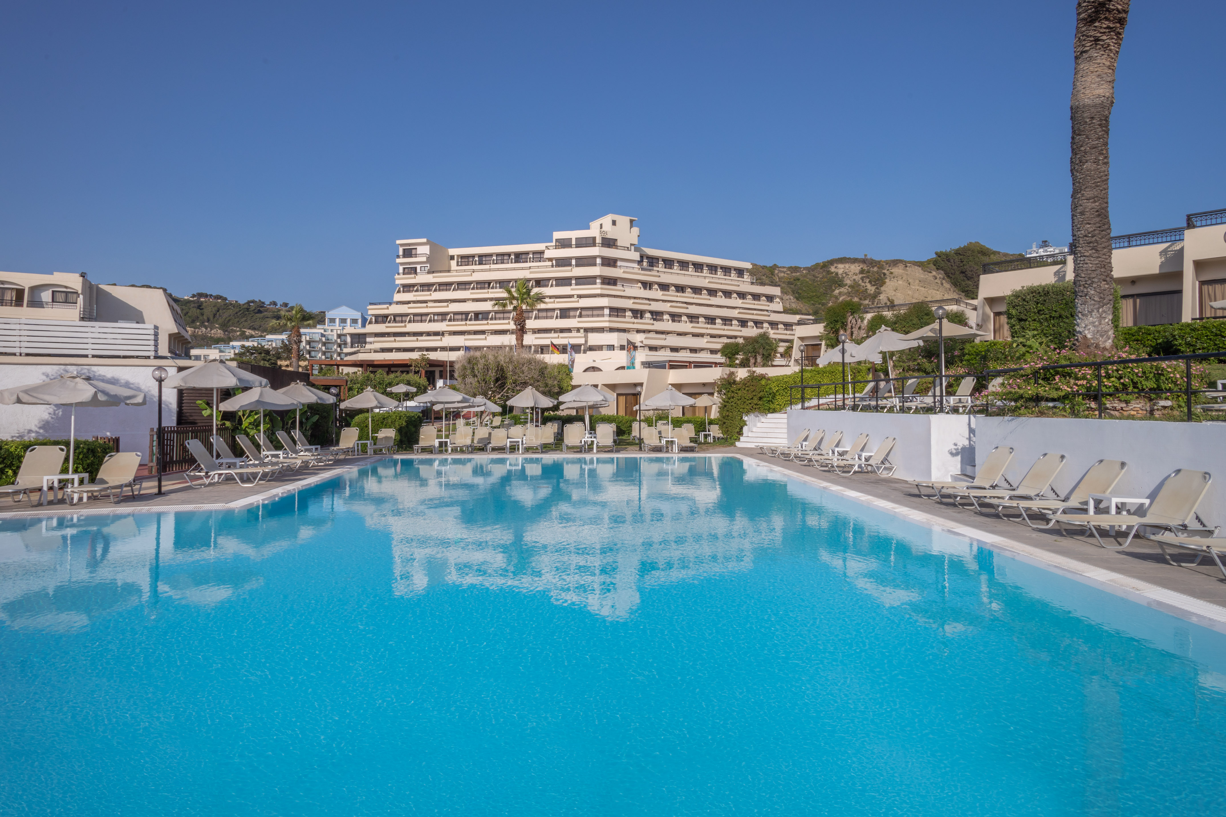 Resort hotel with large outdoor swimming pool, sun loungers, and umbrellas.