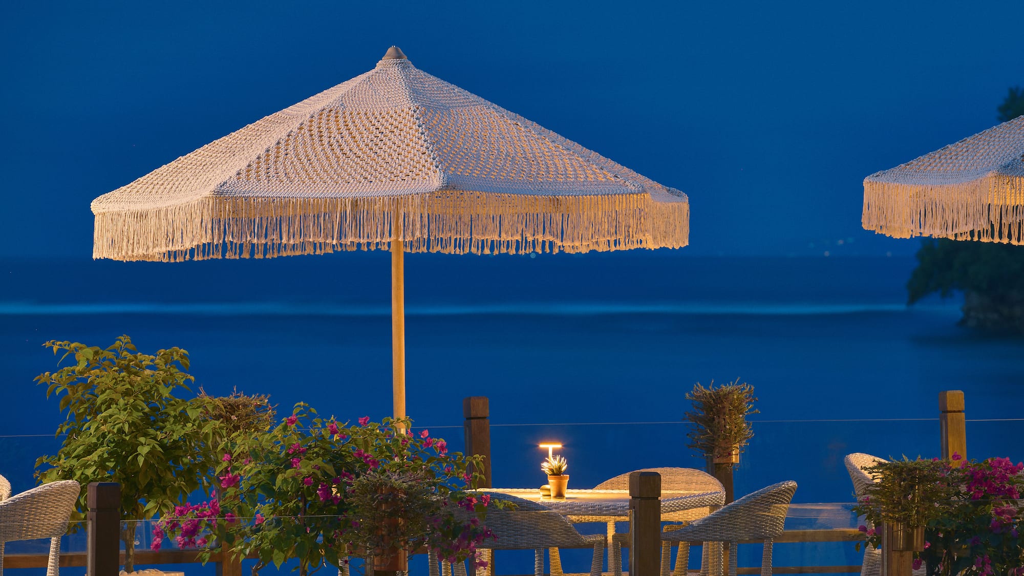 Outdoor dining terrace with macrame umbrellas, sea view at dusk.