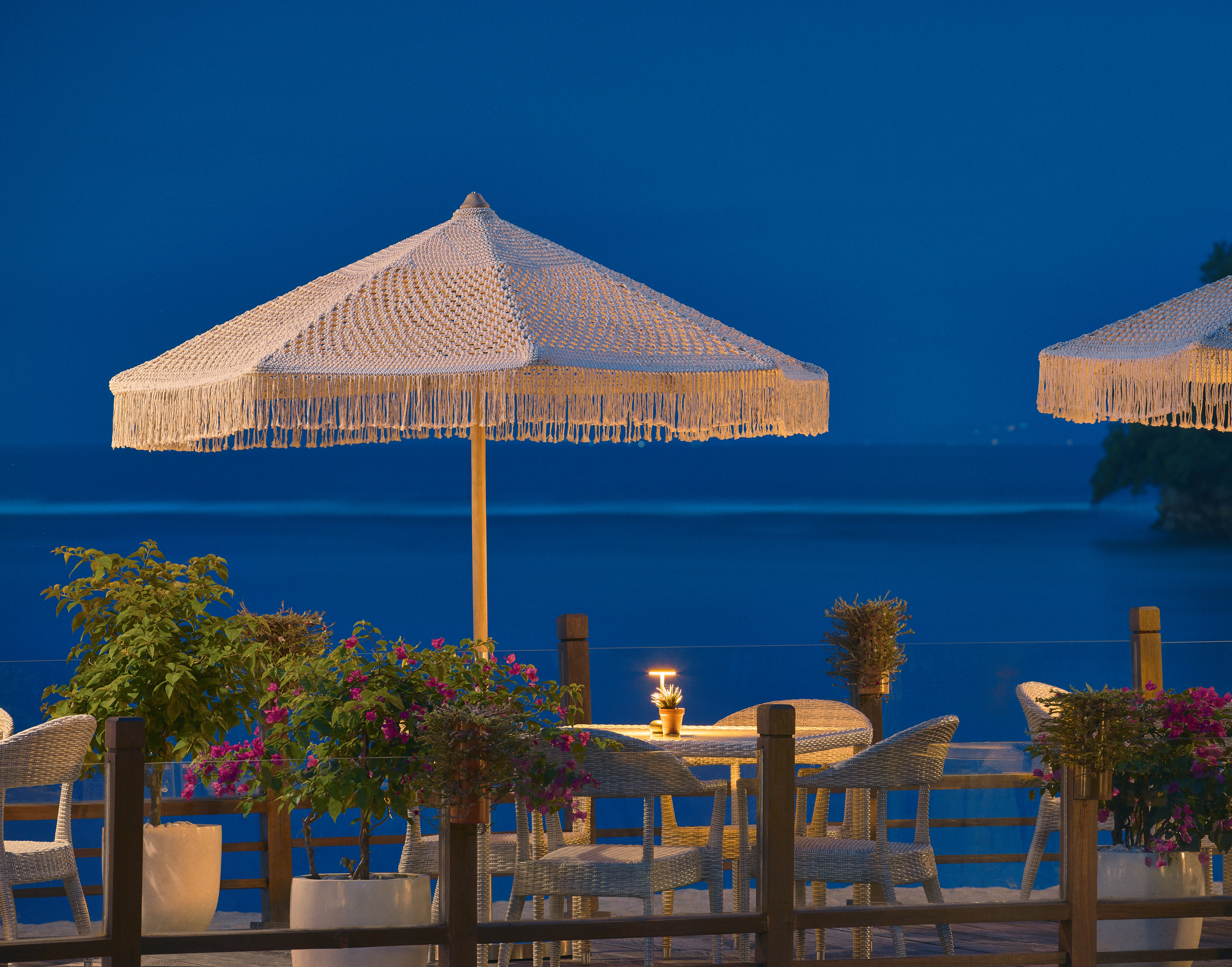 Outdoor dining terrace with macrame umbrellas, sea view at dusk.