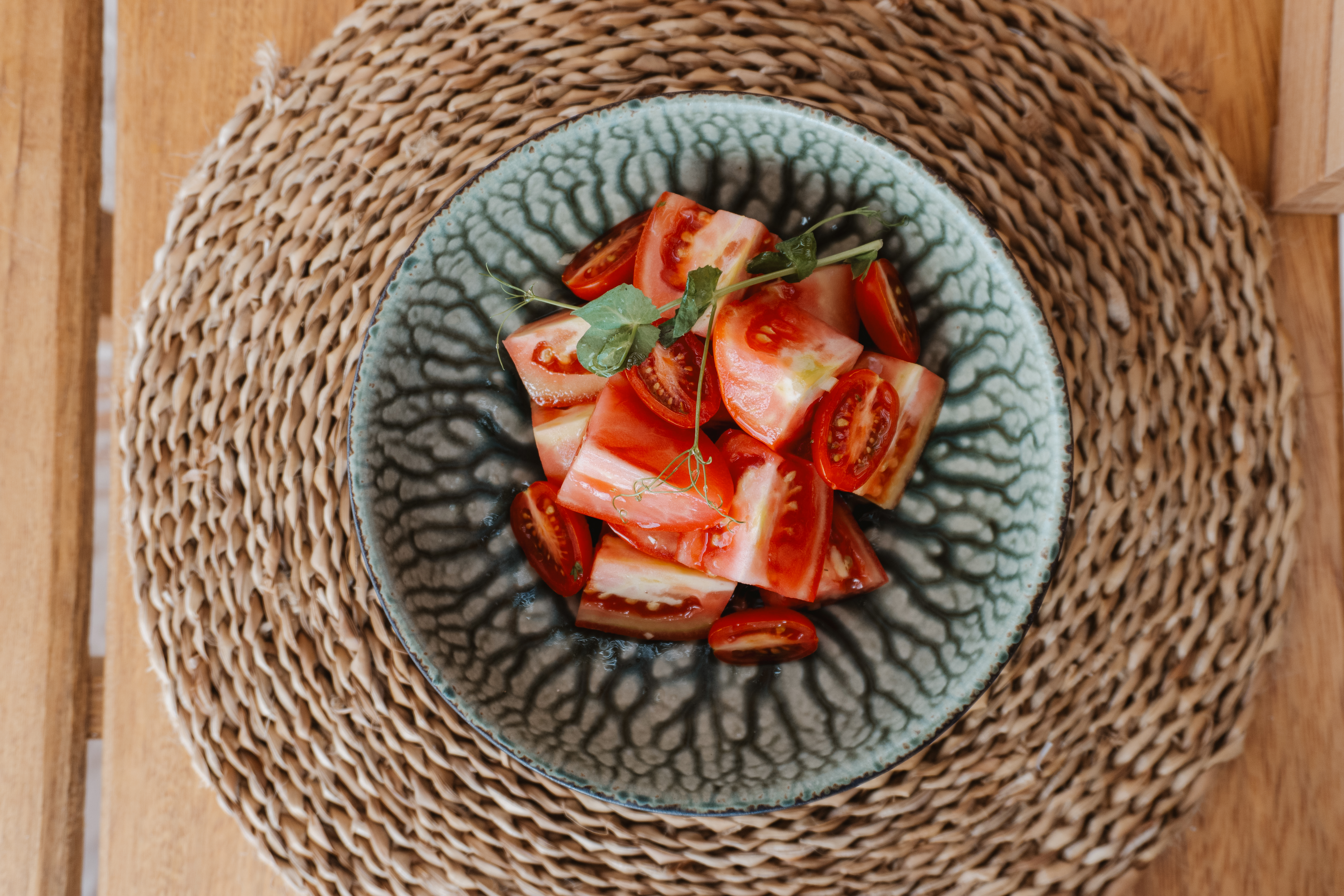 Chopped tomatoes with microgreens in a rustic bowl on a woven placemat.